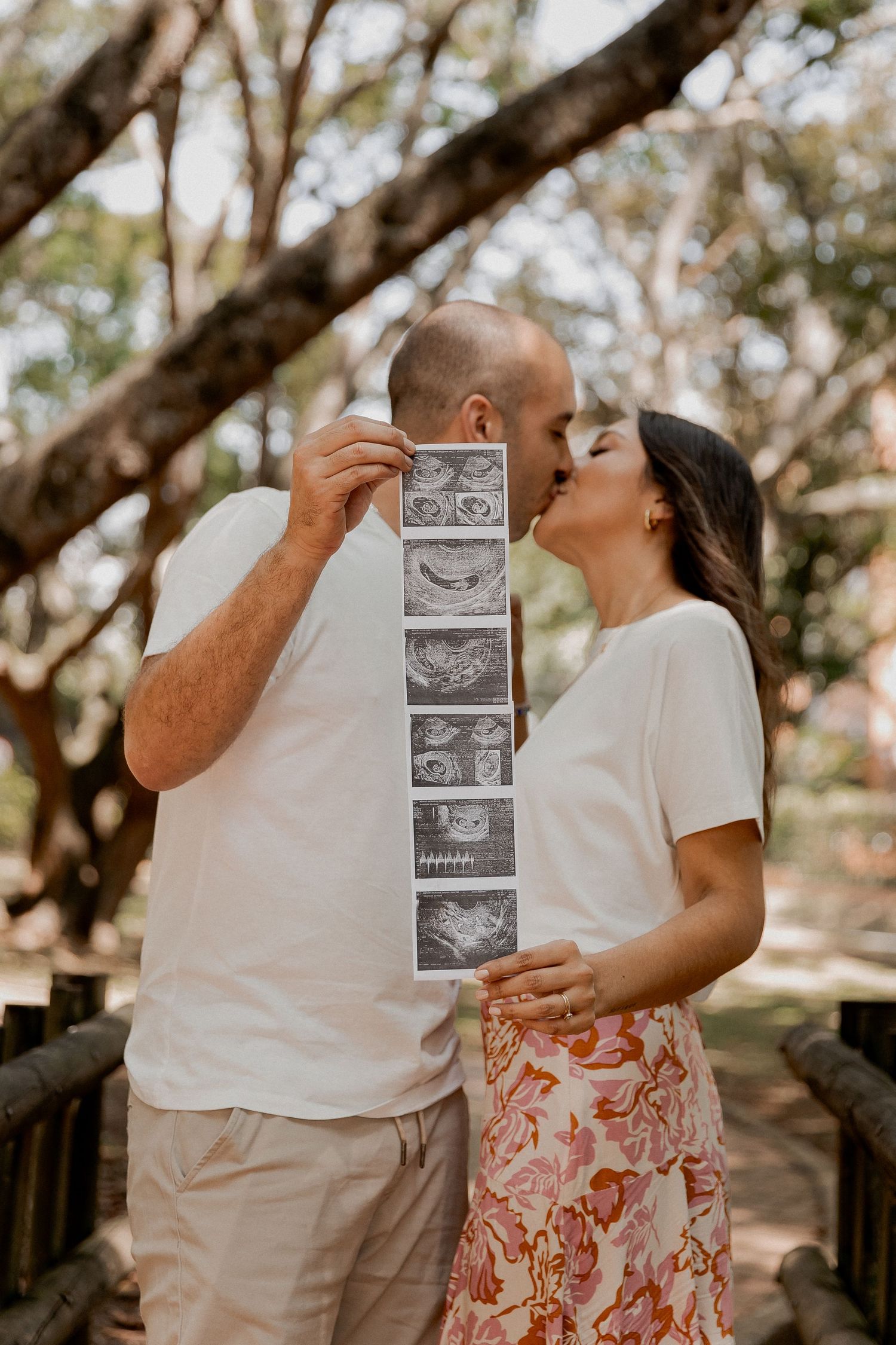 A couple shares ultrasound photos in a sequence of romantic outdoor pregnancy announcement photos.