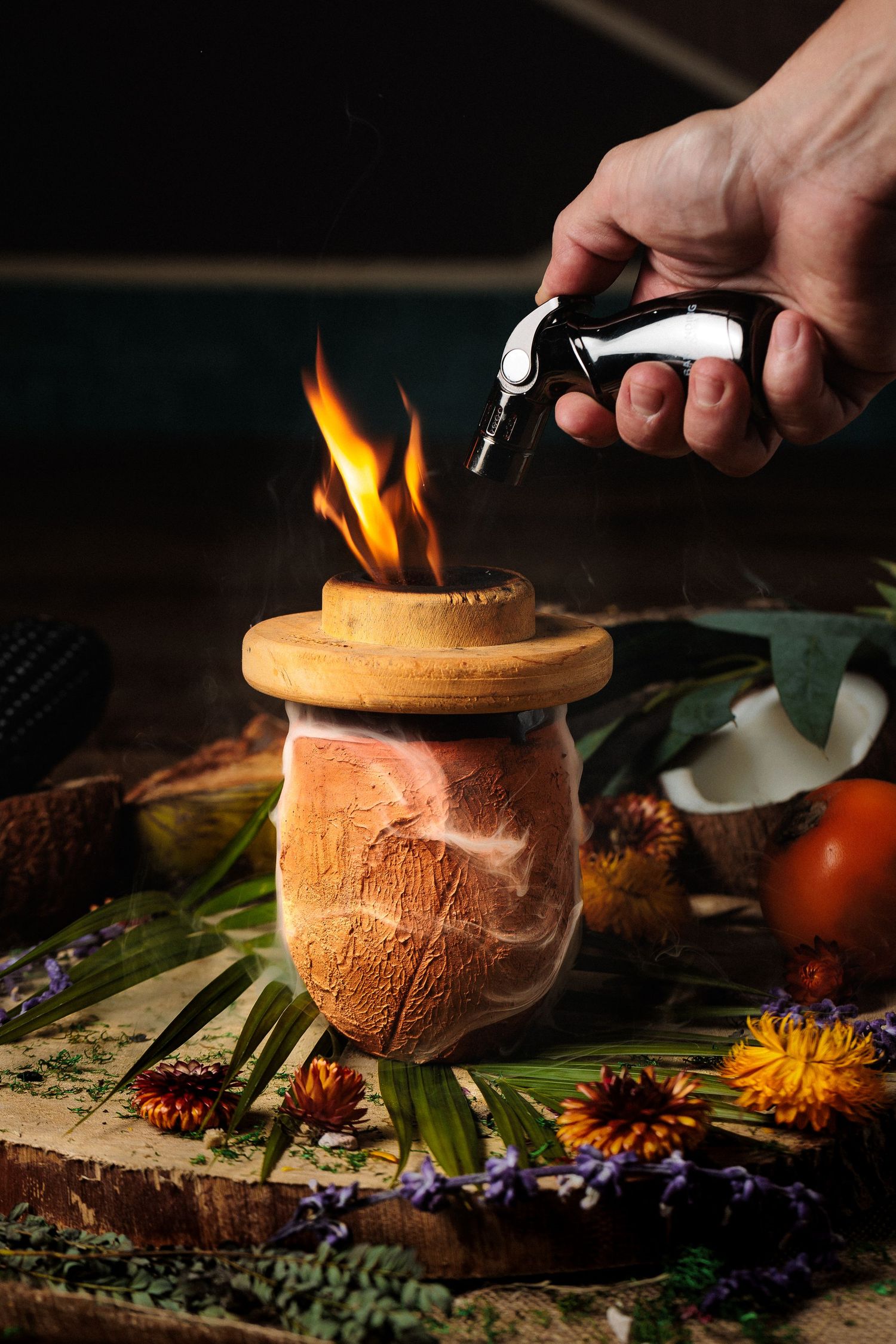 A torch flame is used to caramelize the top of a coconut dessert served on tropical leaves with flowers and citrus fruits.