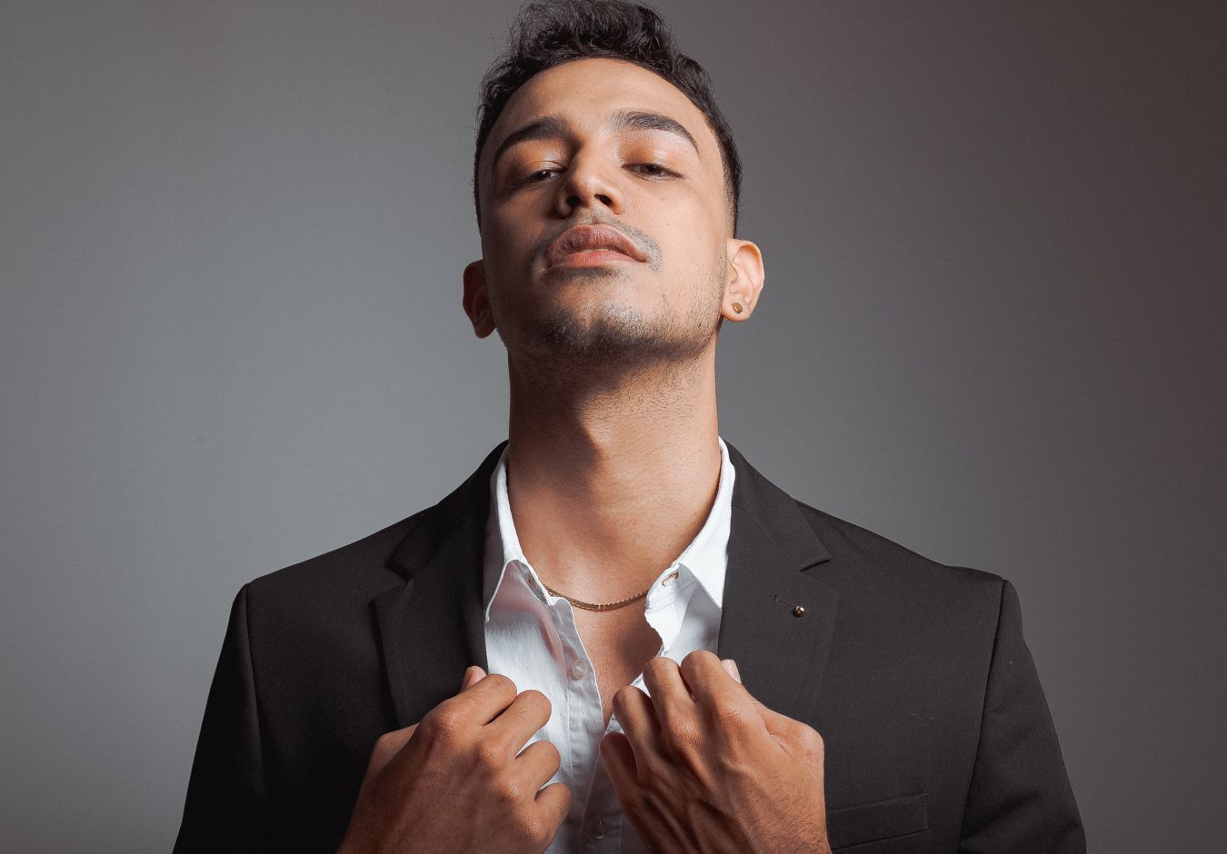 Professional studio portrait series showing dramatic angles and poses of someone wearing a black suit against a gray backdrop.
