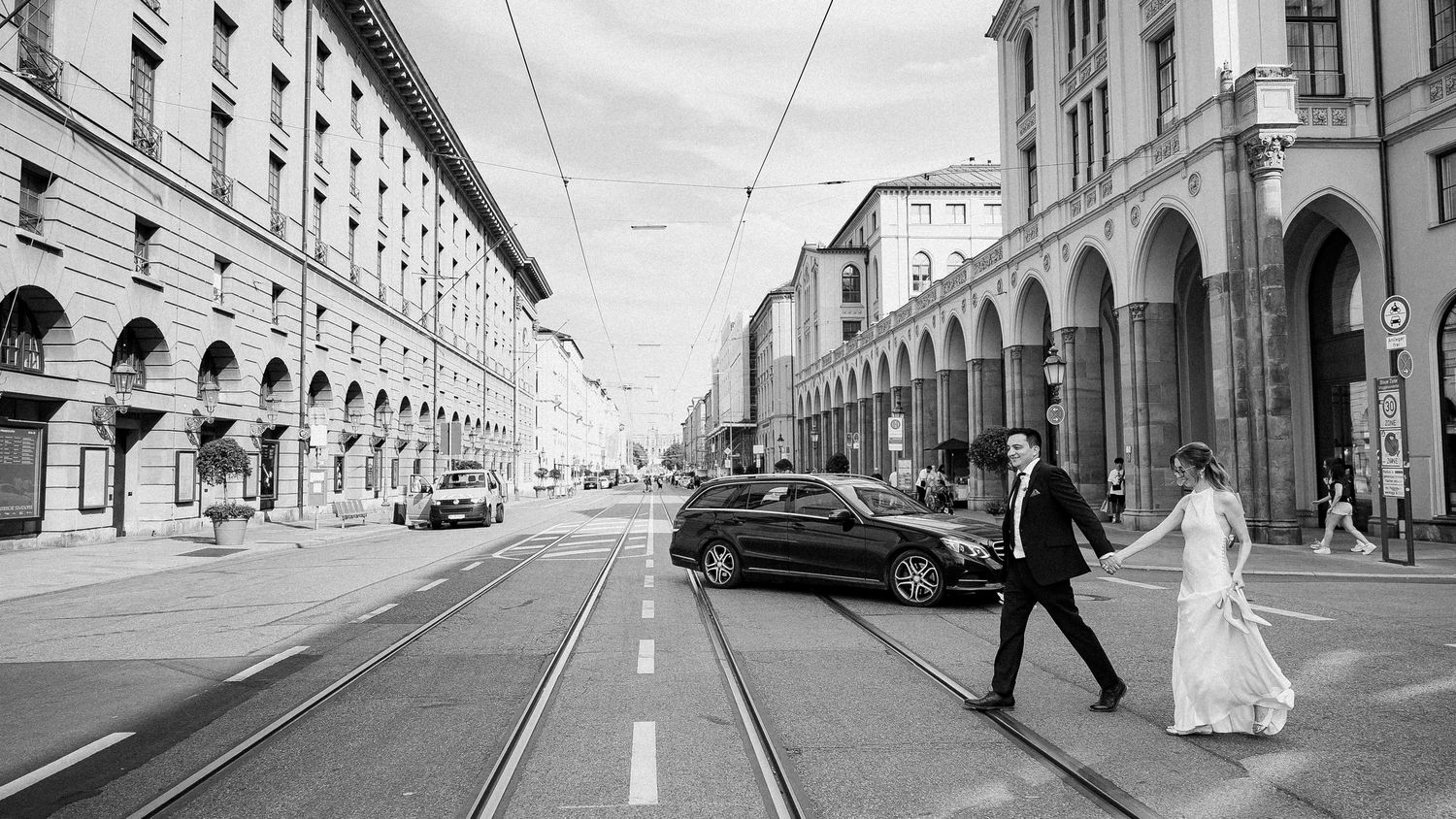 Bride and groom crossing a city street with tram tracks in black and white wedding photo.