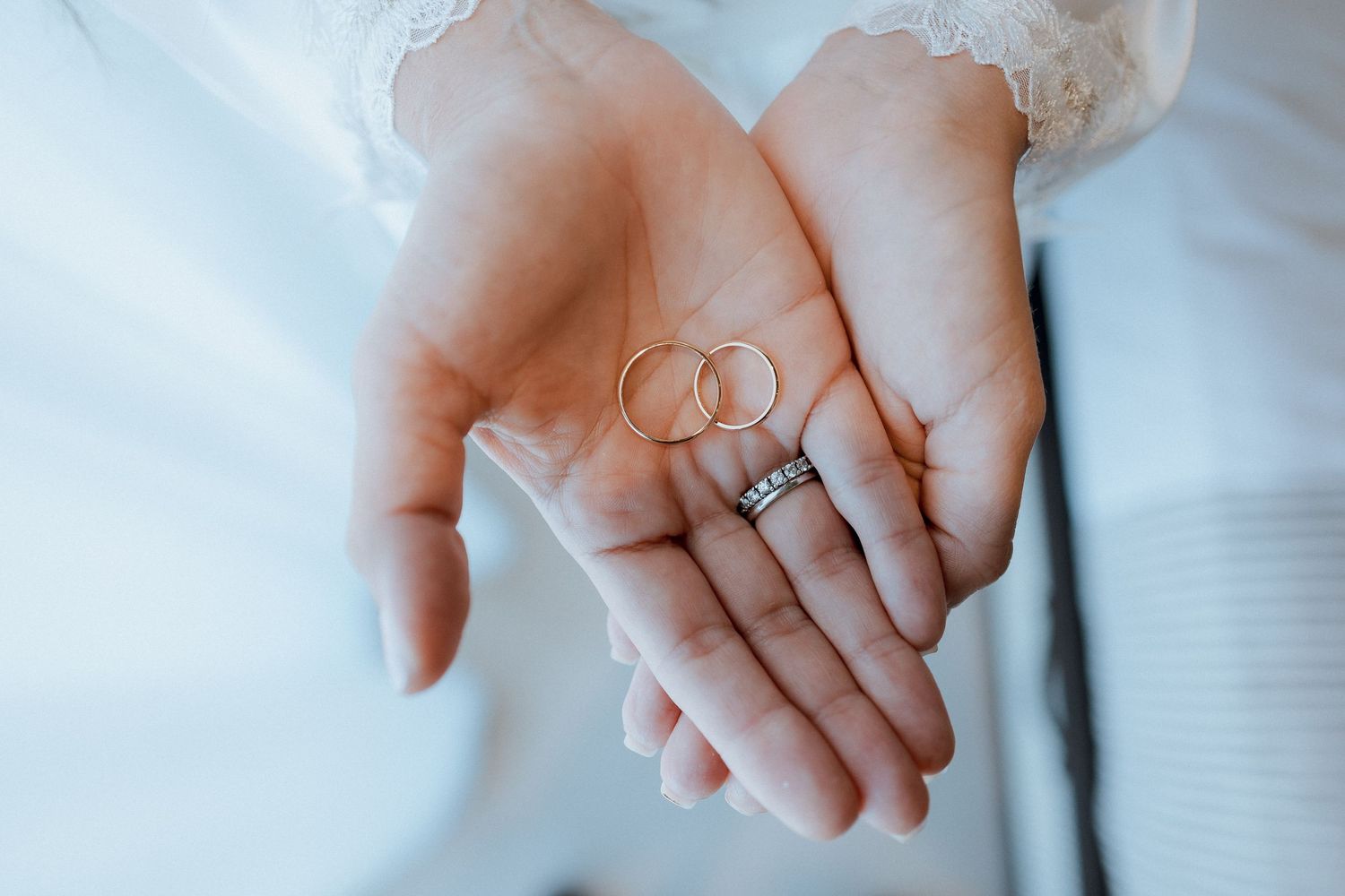 Hands holding two gold wedding rings with a diamond ring on finger, close-up bridal jewelry photo.