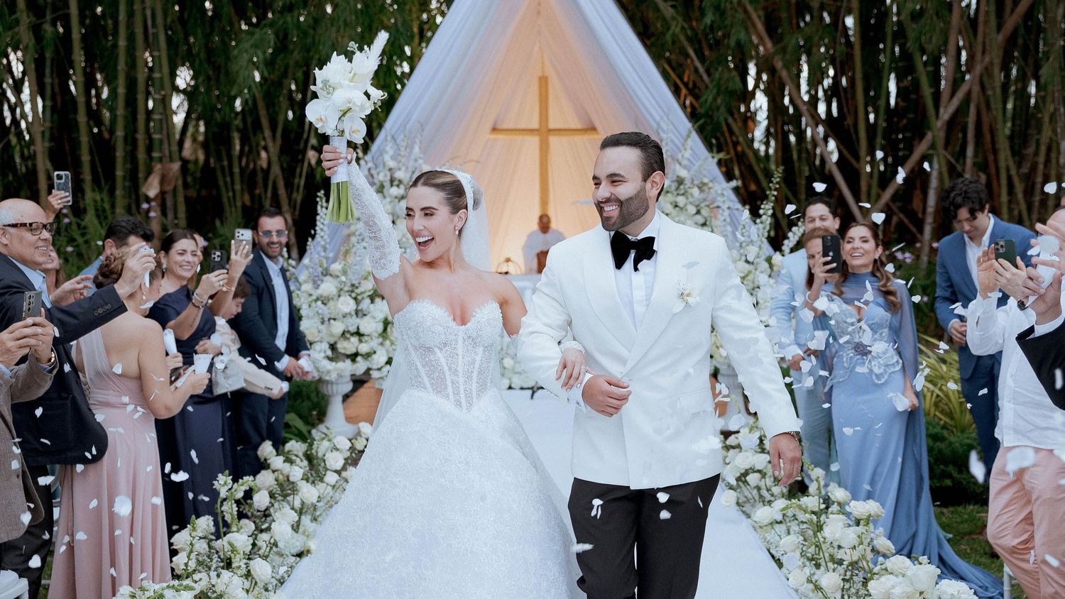 Wedding guests dance and celebrate on a lush garden dance floor decorated with white floral arrangements.