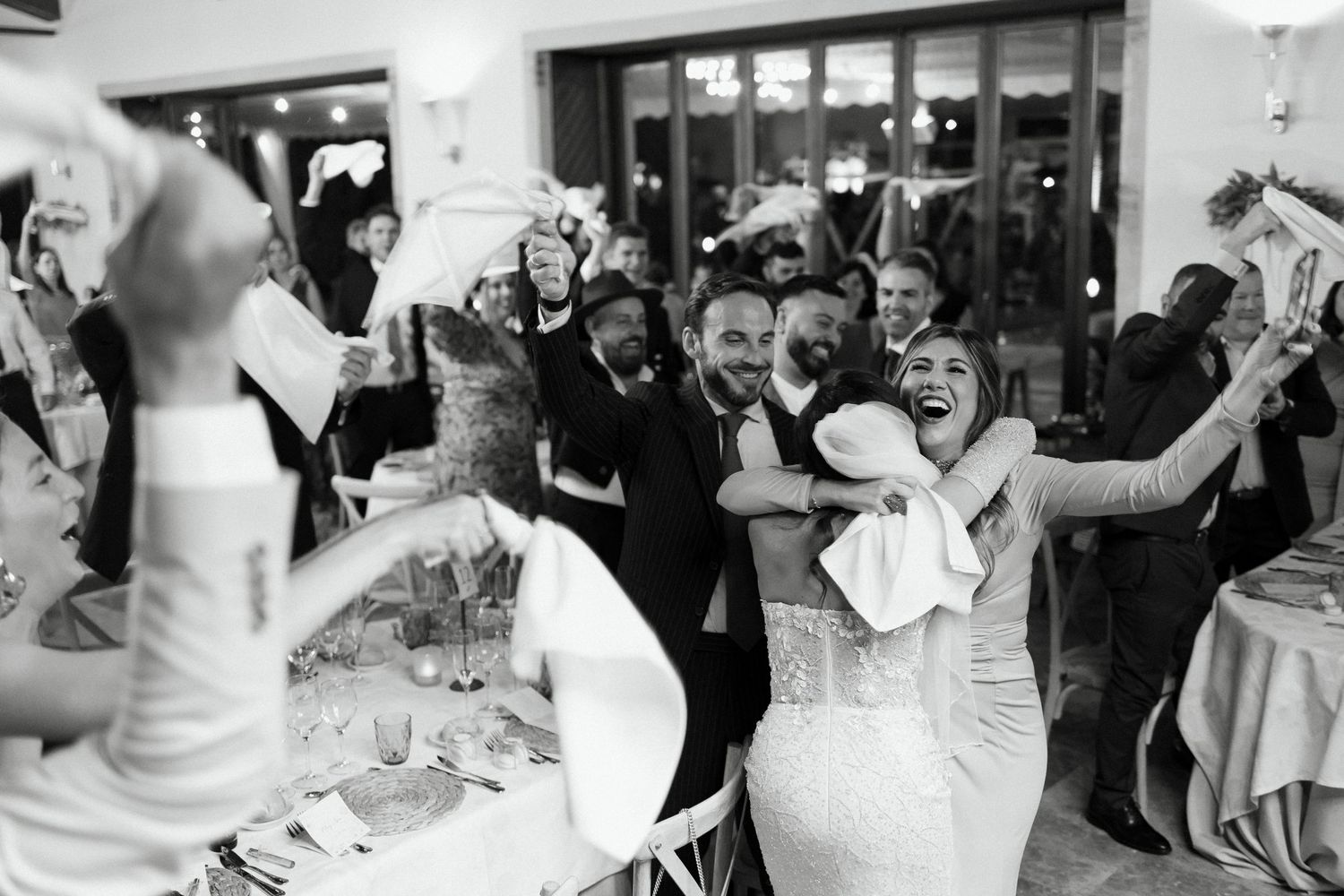 Black and white photo of joyful bride and groom celebrating with guests at a lively wedding reception.