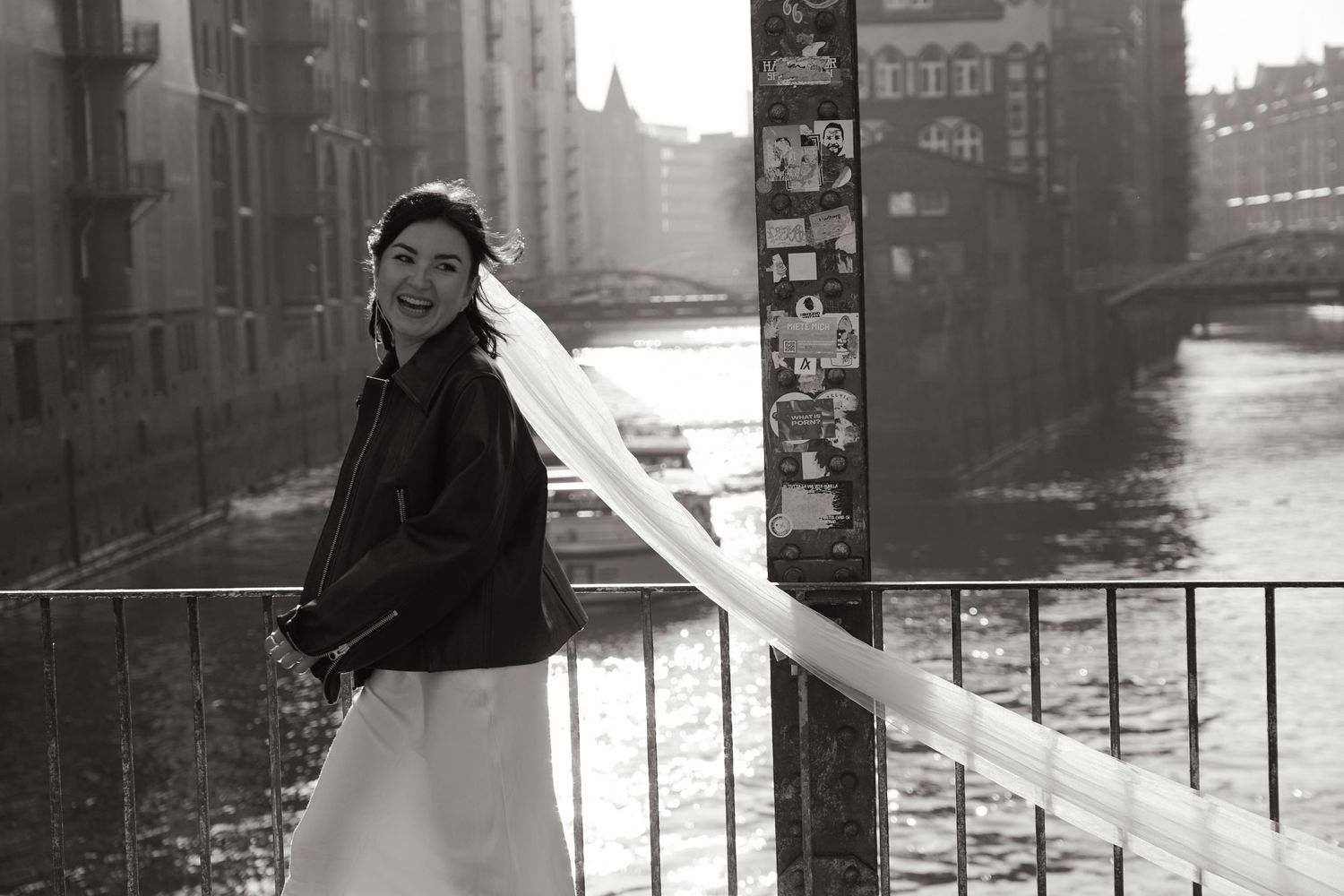 Black and white portrait of bride in winter coat along urban waterfront.