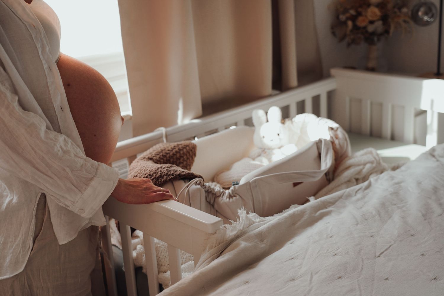 Detail shot of hands preparing white baby crib with soft linens.