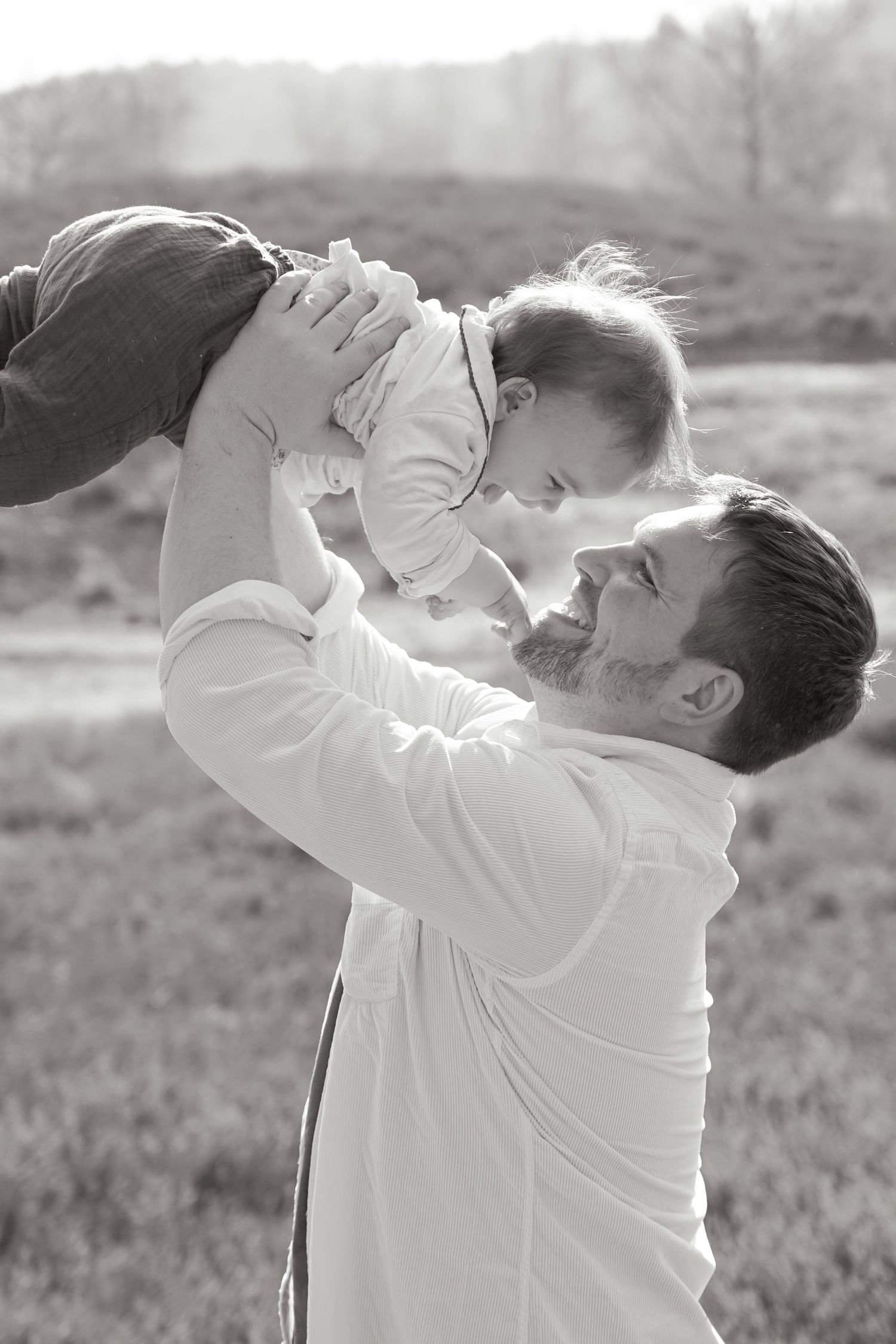 A tender outdoor moment between a parent and child playing together in a grassy field, captured in black and white.