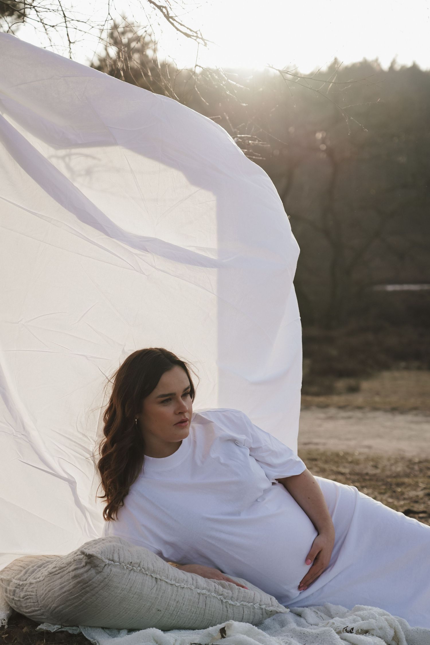 A maternity photo with flowing white fabric in an outdoor setting at sunset.