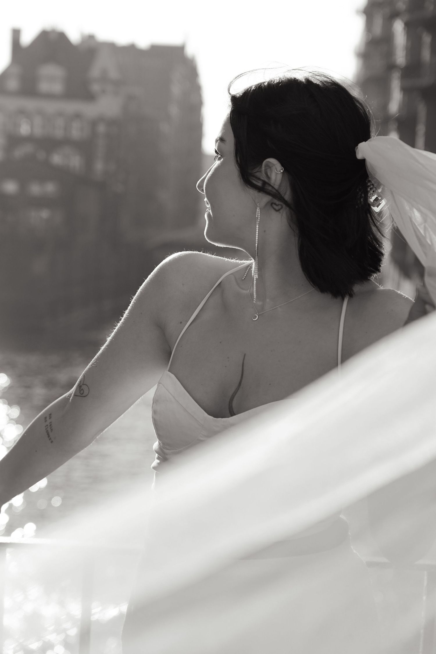 Artistic black and white profile shot of a bride with flowing veil against urban architecture.