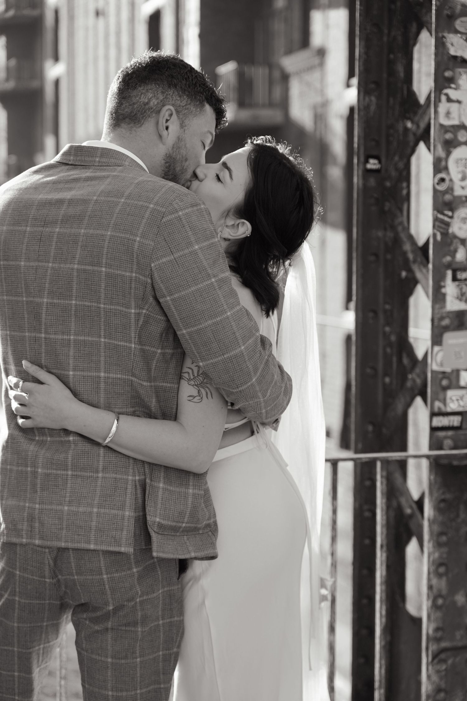 A romantic embrace between newlyweds, with the groom wearing a checkered suit and bride in white.