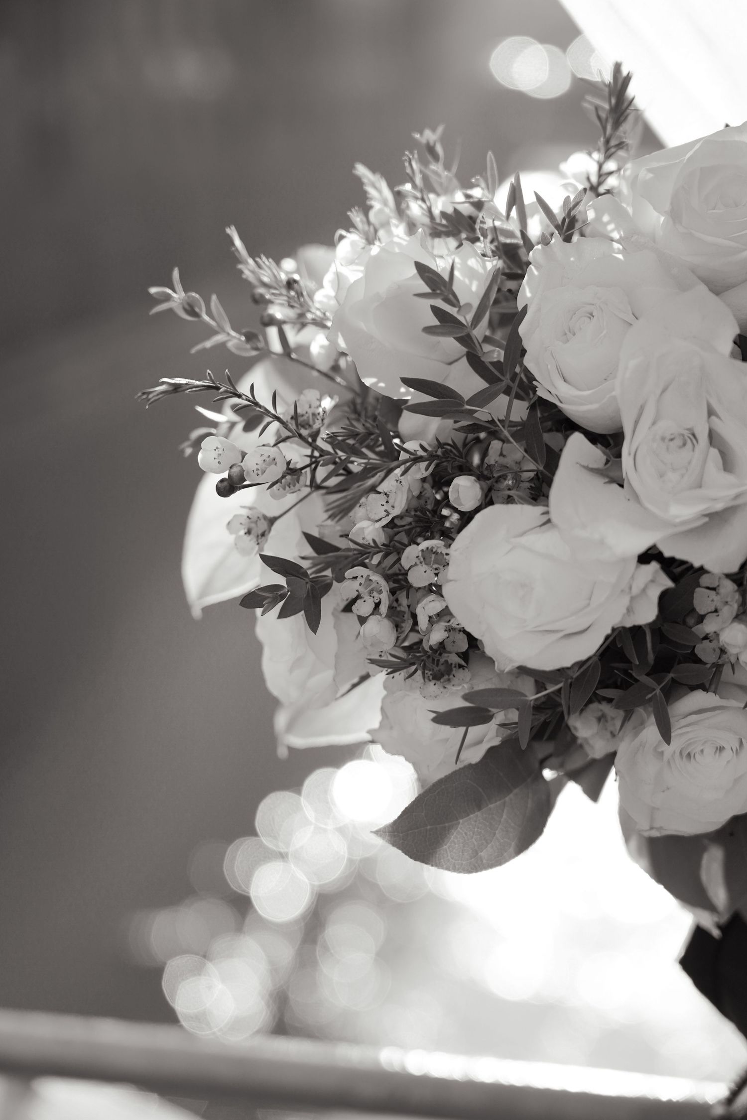 Elegant wedding bouquet with white roses and greenery captured in black and white with bokeh background.