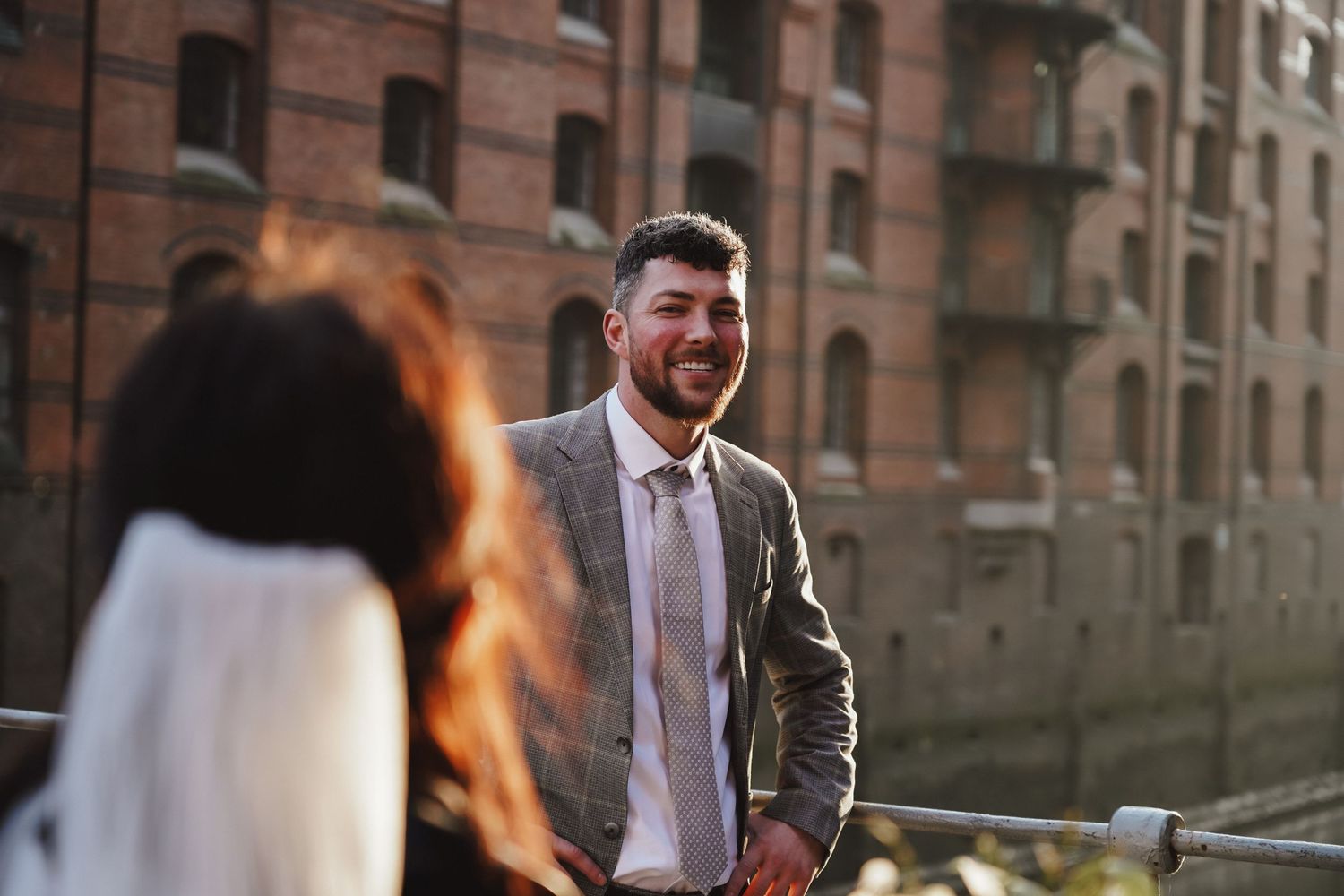 Romantic urban wedding photo with brick building backdrop in warm evening light.