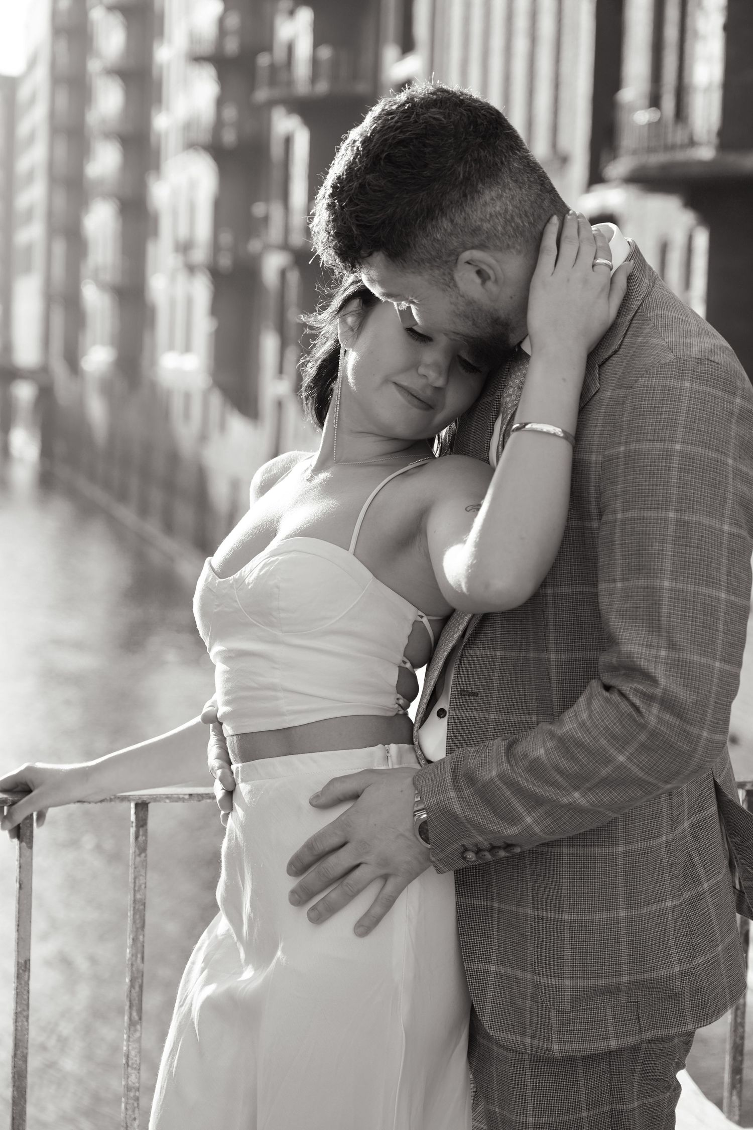 A romantic black and white photo of a couple embracing in a cropped top and plaid blazer.