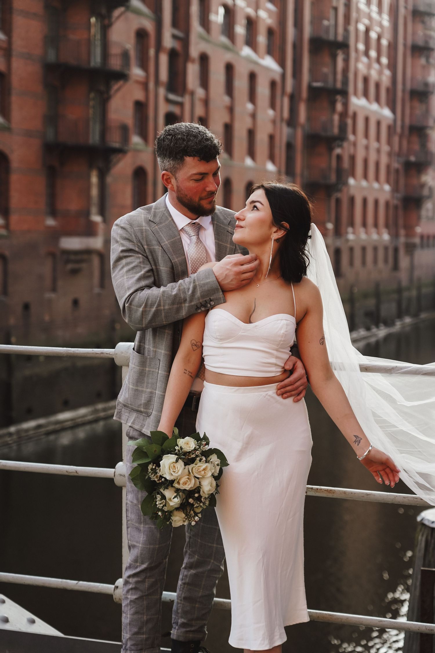 Romantic wedding portrait with couple posing against historic brick architecture.