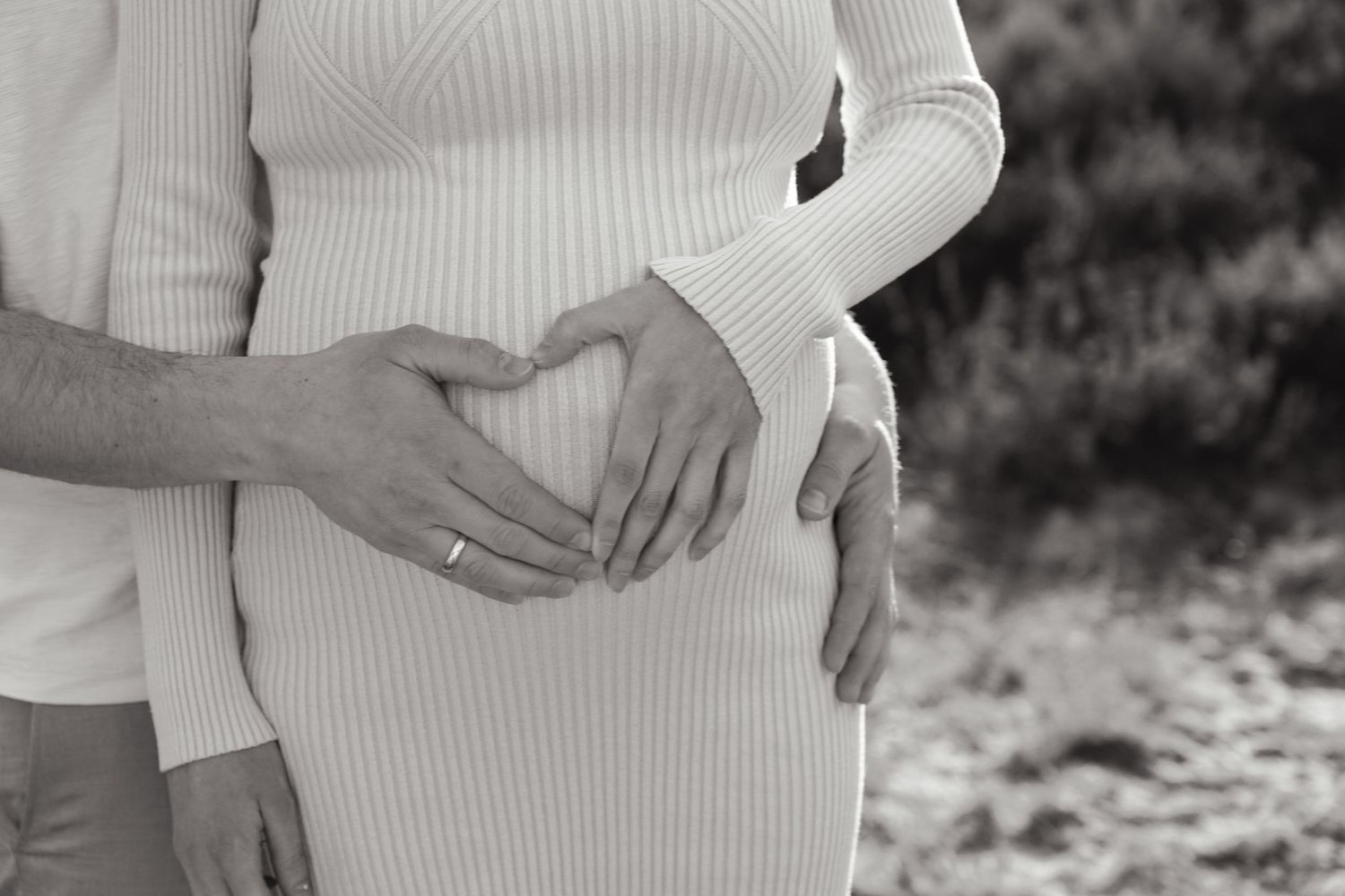 Close-up black and white photo showing hands cradling a pregnant belly in a ribbed sweater.