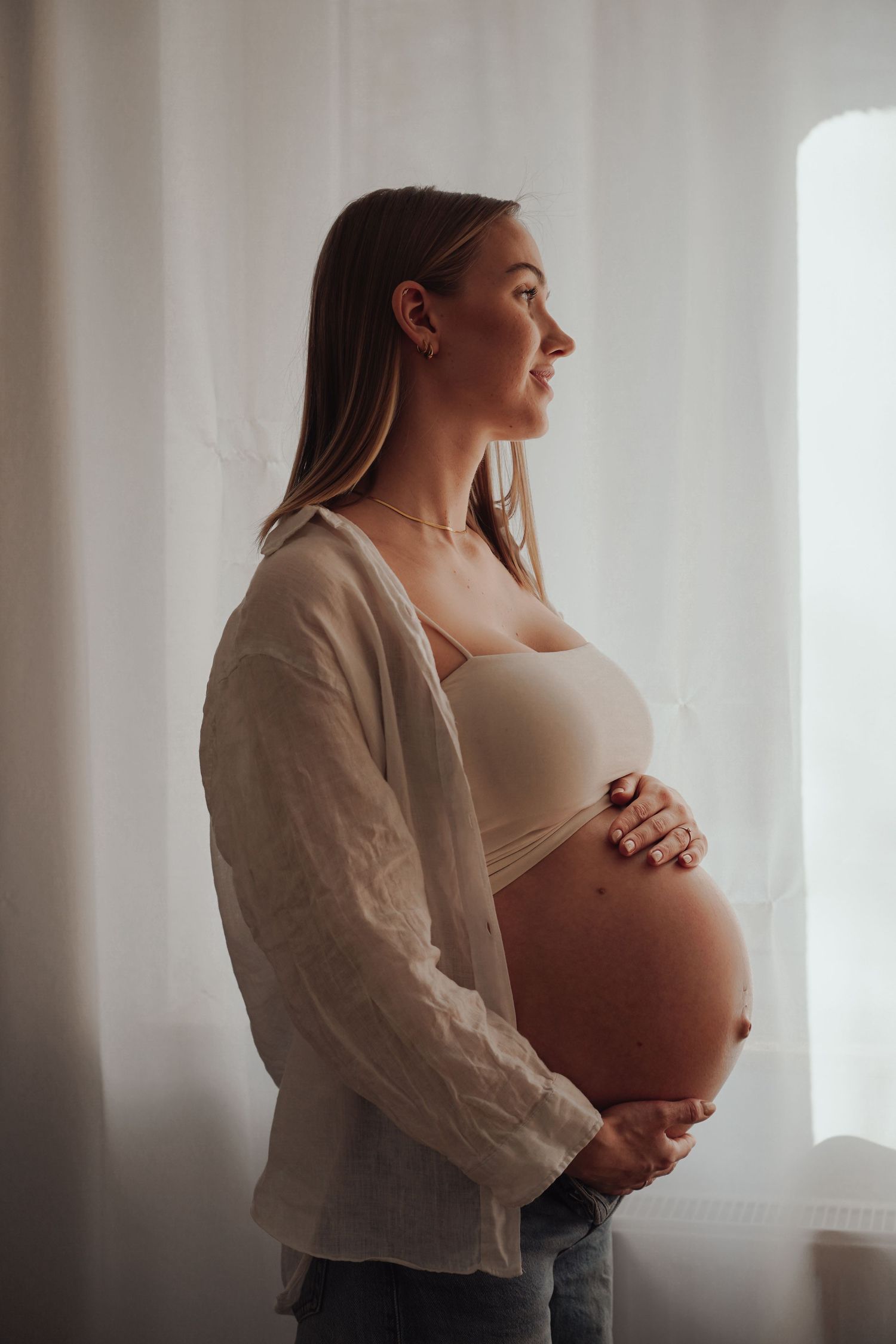 Side profile maternity portrait in natural window light wearing casual attire.