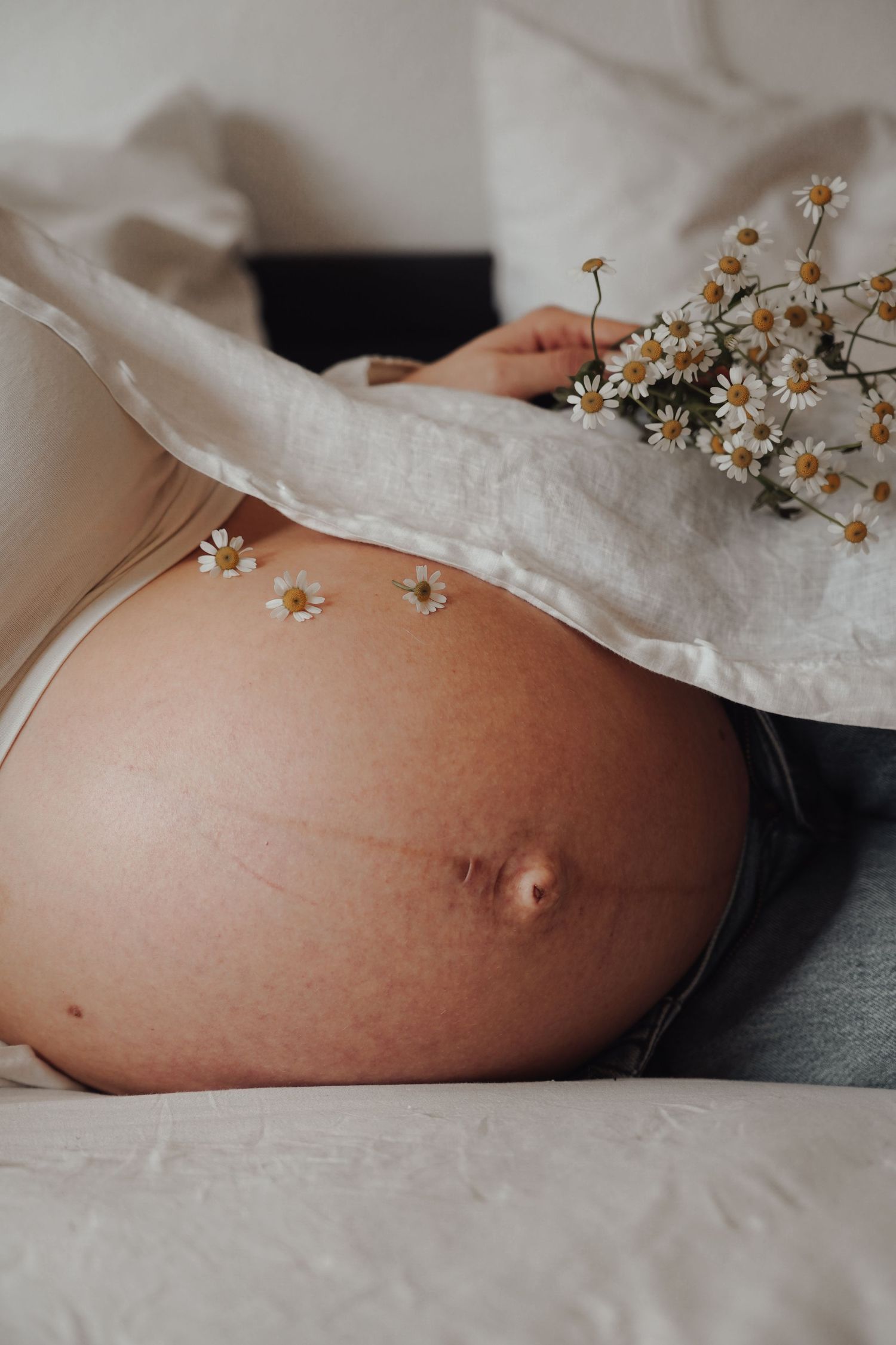 Artistic maternity photo with delicate white flowers resting on pregnant belly.