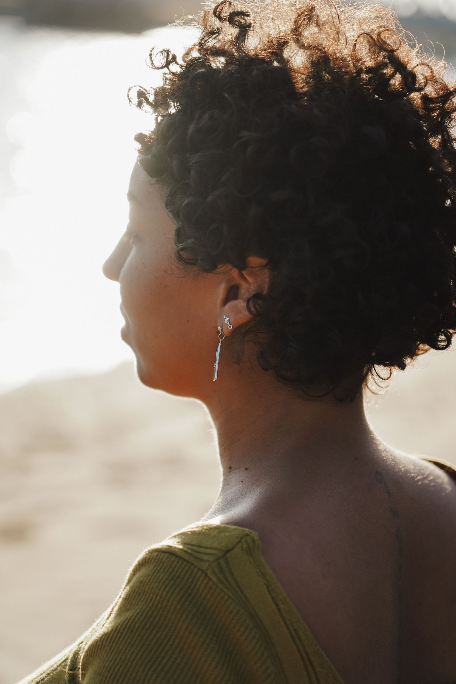 Profile portrait showing curly hair and earring silhouetted against warm sunlight.
