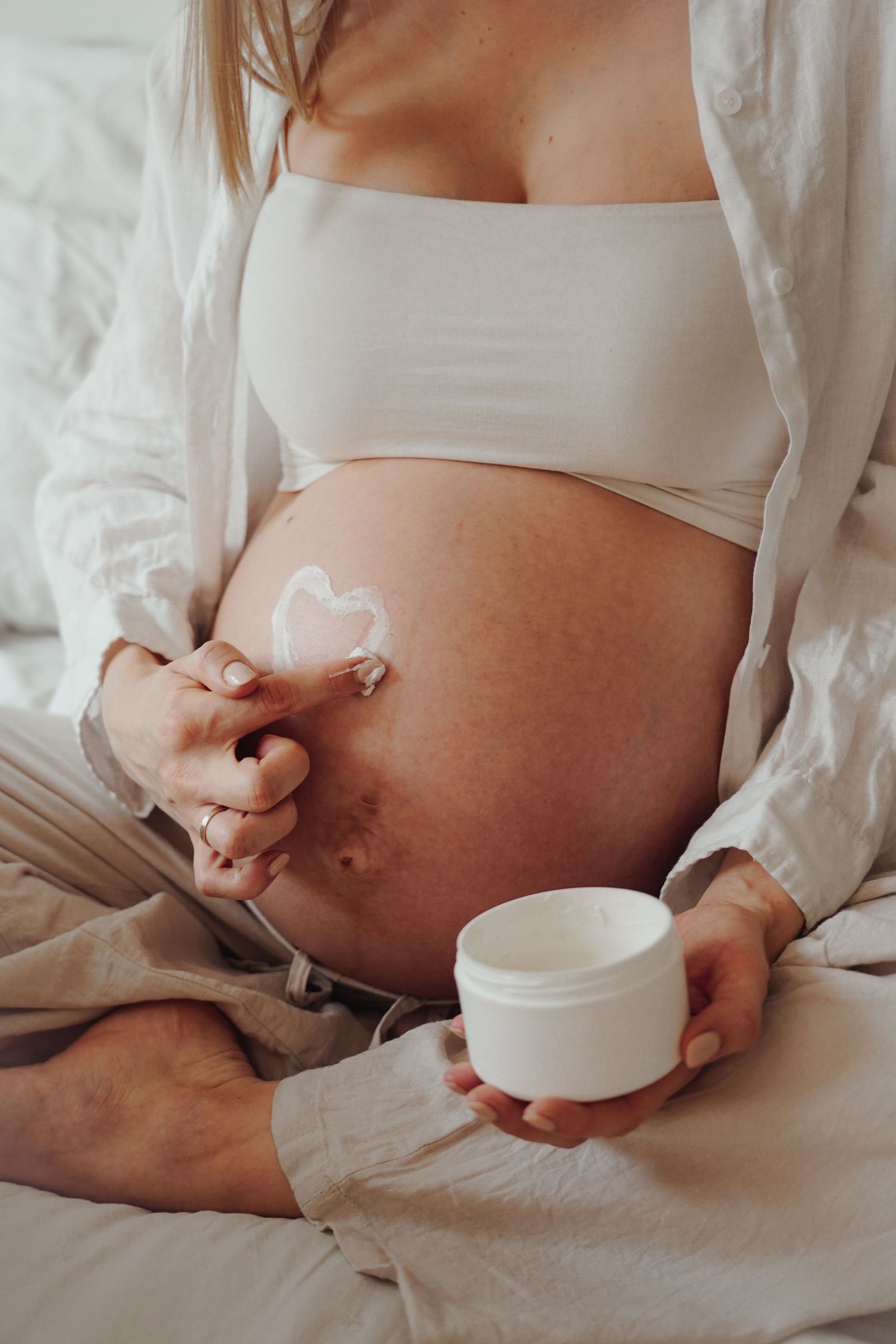 Close-up of pregnant belly with heart drawn in cream while holding moisturizer.