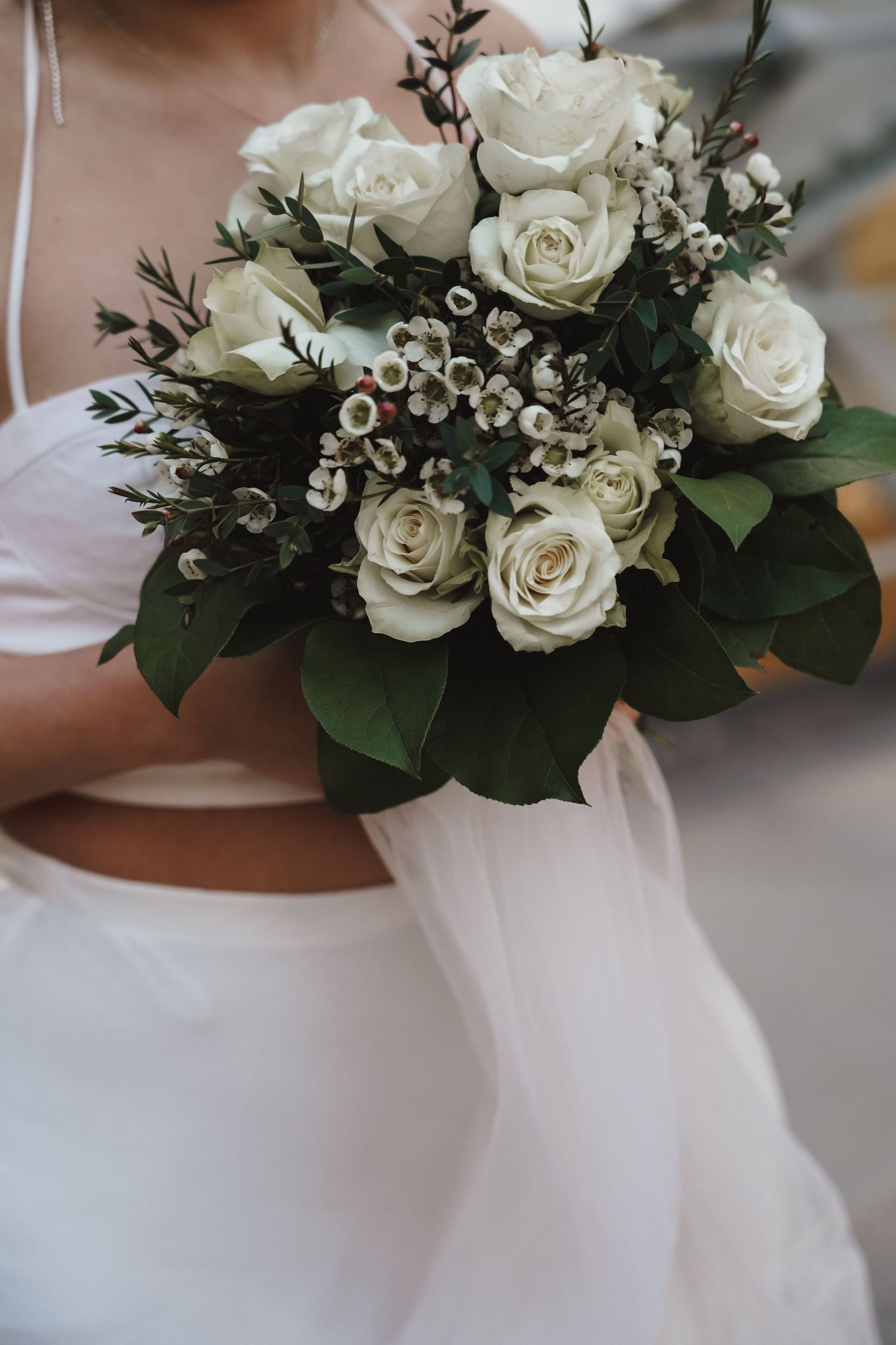 A classic white bridal bouquet with roses and greenery against a white dress.