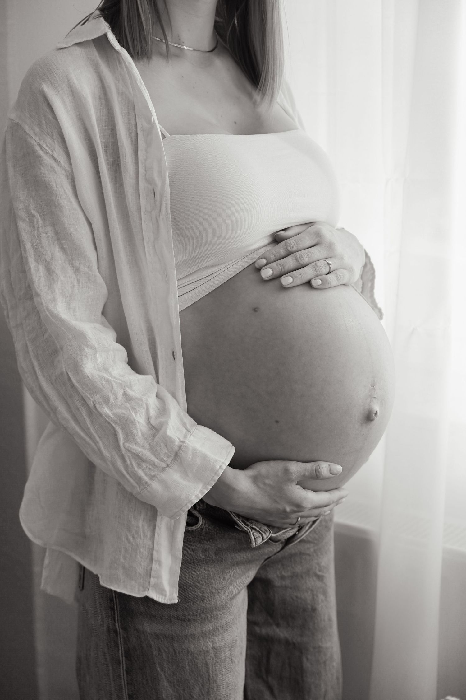 Monochrome portrait of a pregnant woman wearing an oversized white shirt and jeans.