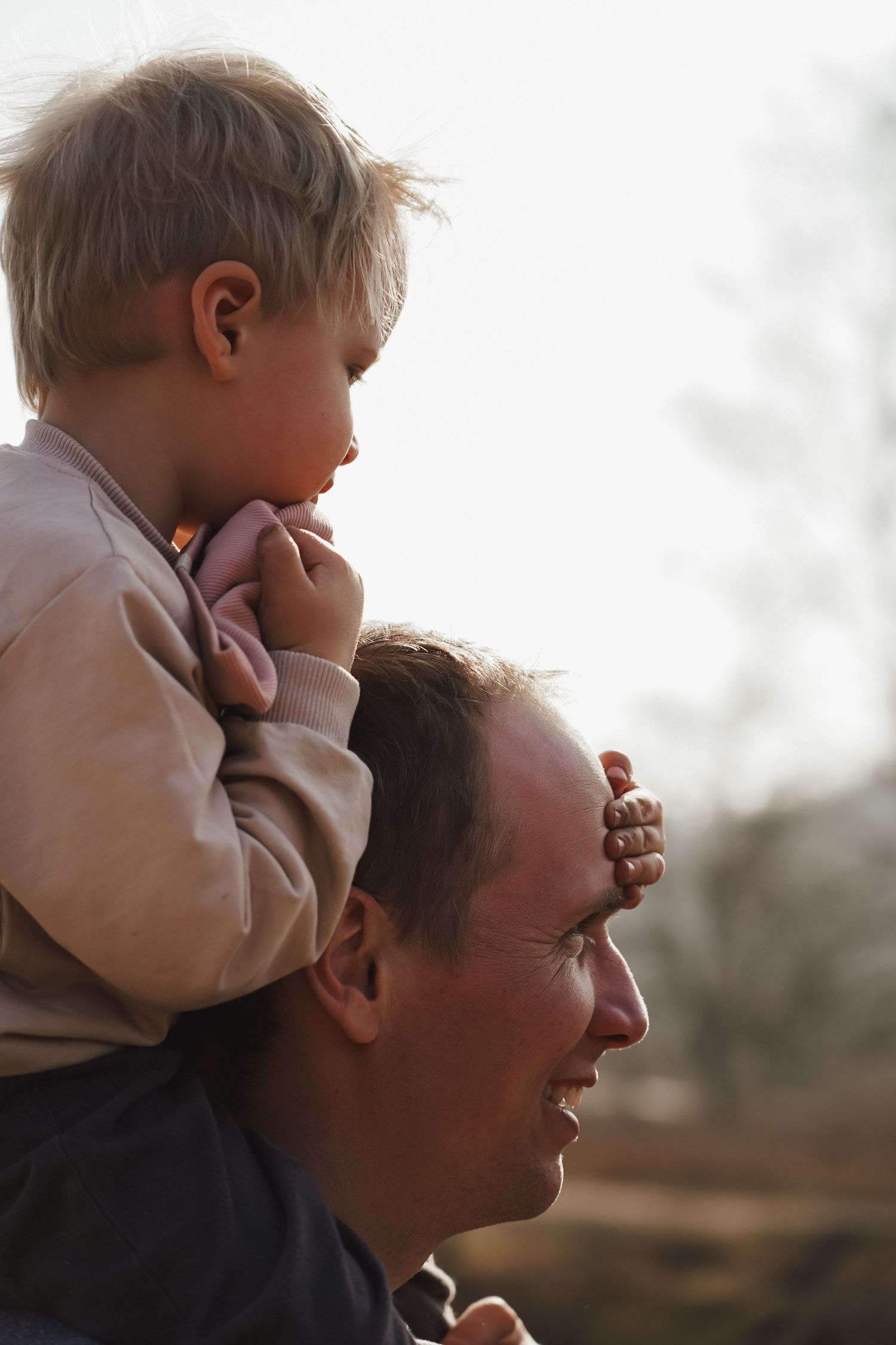 Child sits on shoulders during sunset creating silhouette against bright sky.