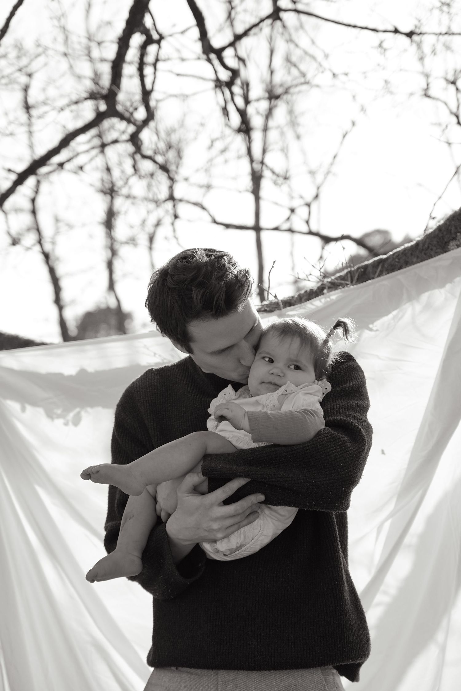 An intimate black and white portrait against white fabric and bare tree branches.