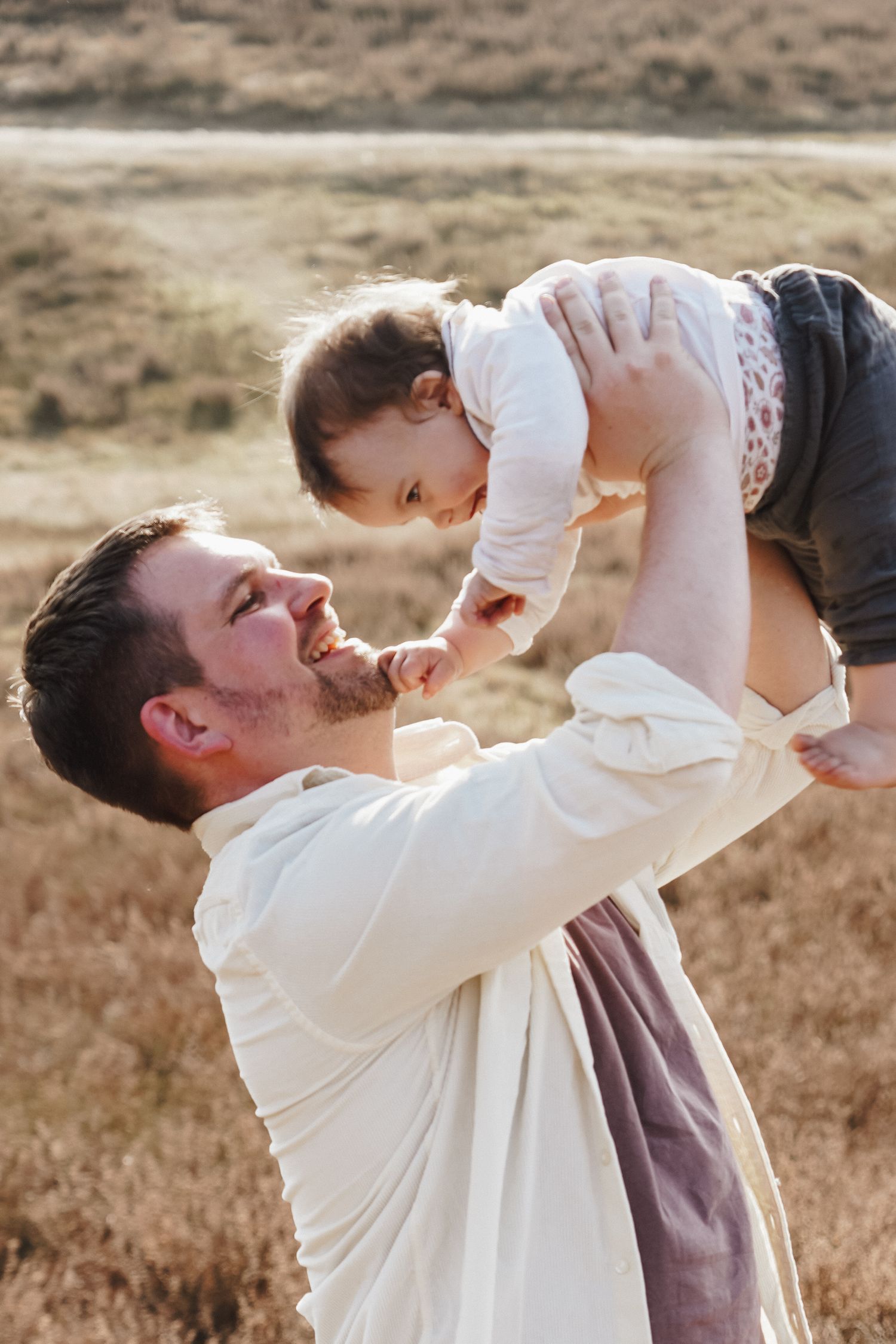 A joyful moment captured as a toddler is lifted high in the air outdoors.