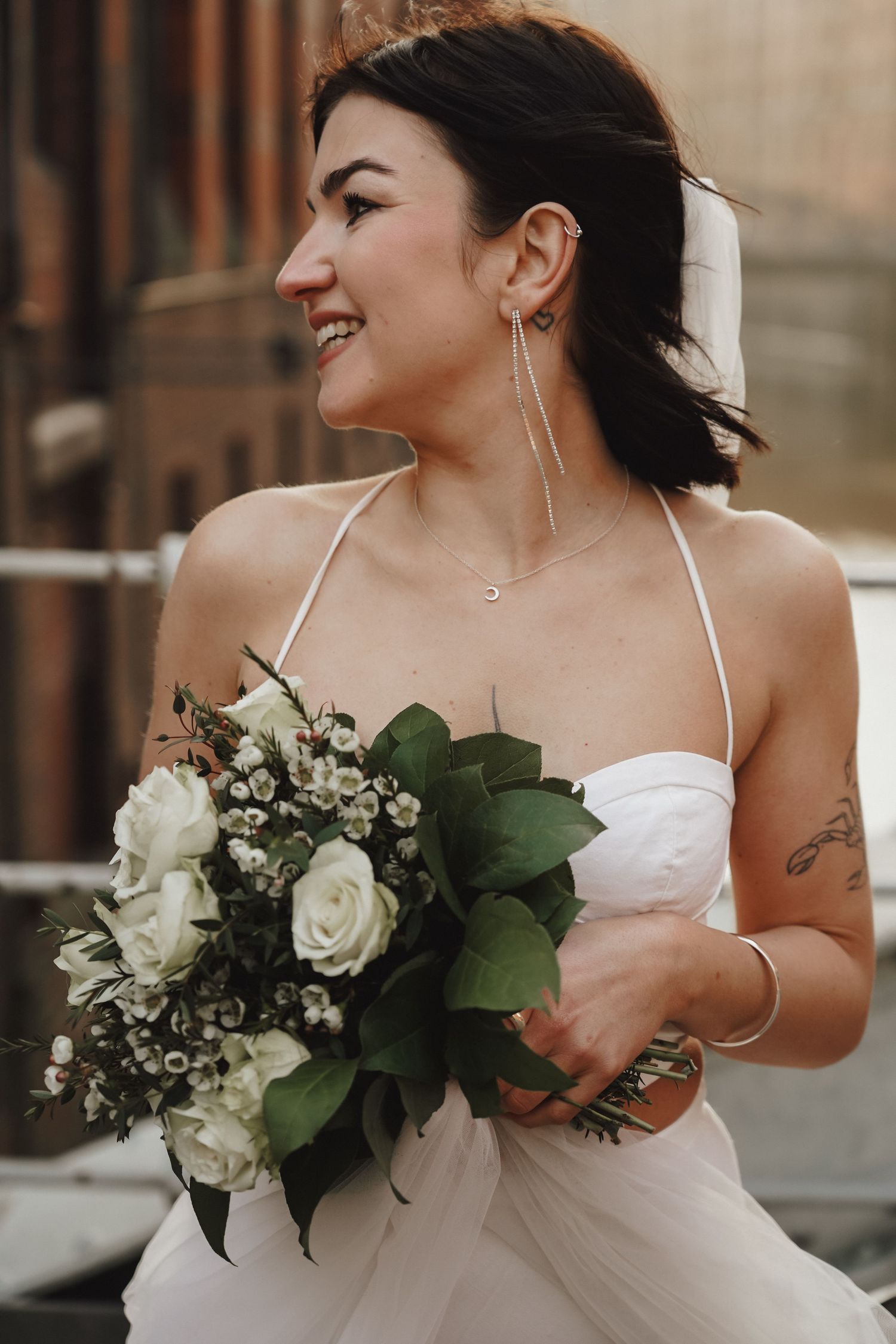 Bride in modern two-piece dress holding white rose bouquet while smiling.