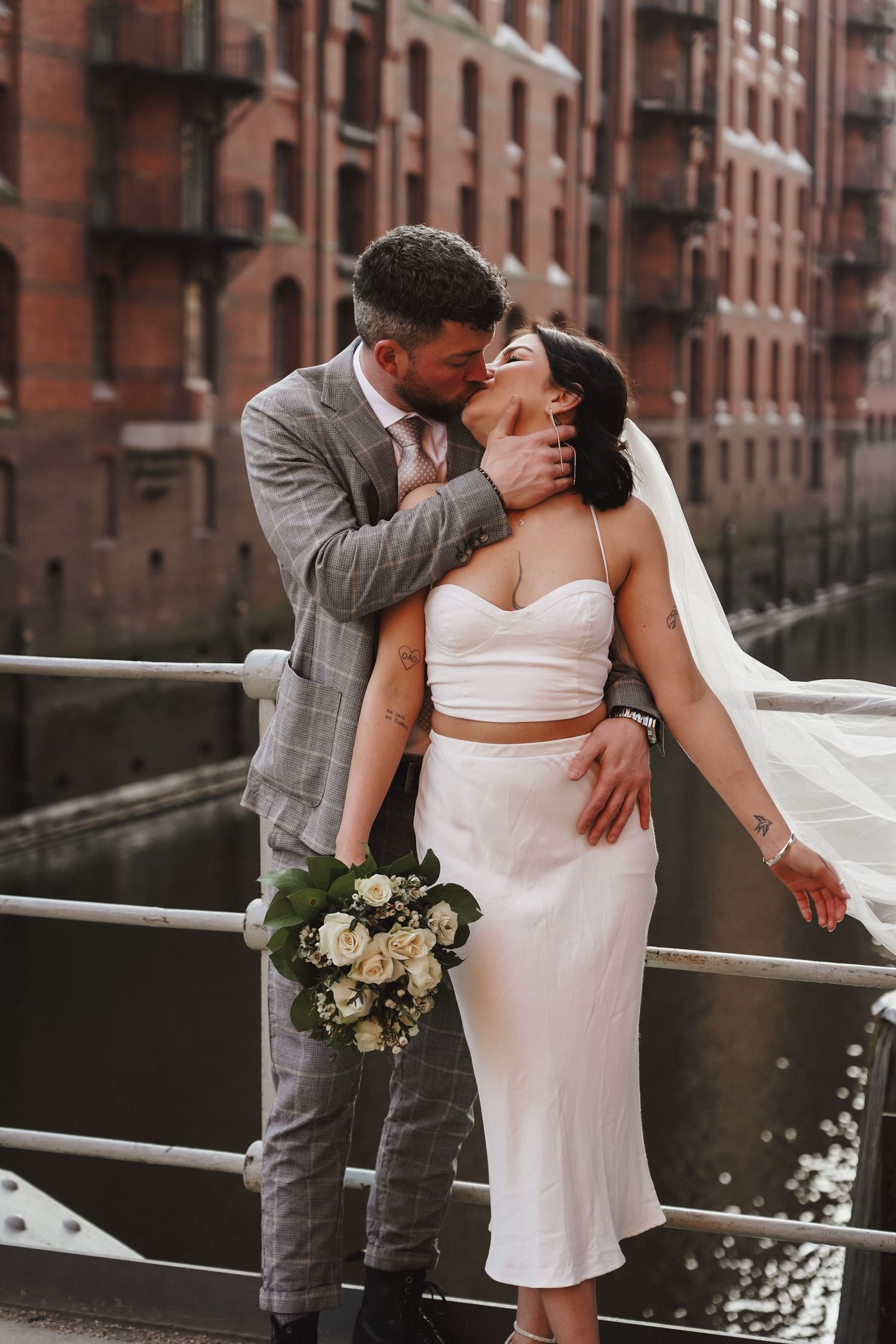 Romantic wedding photo with bride holding bouquet against historic waterfront architecture.