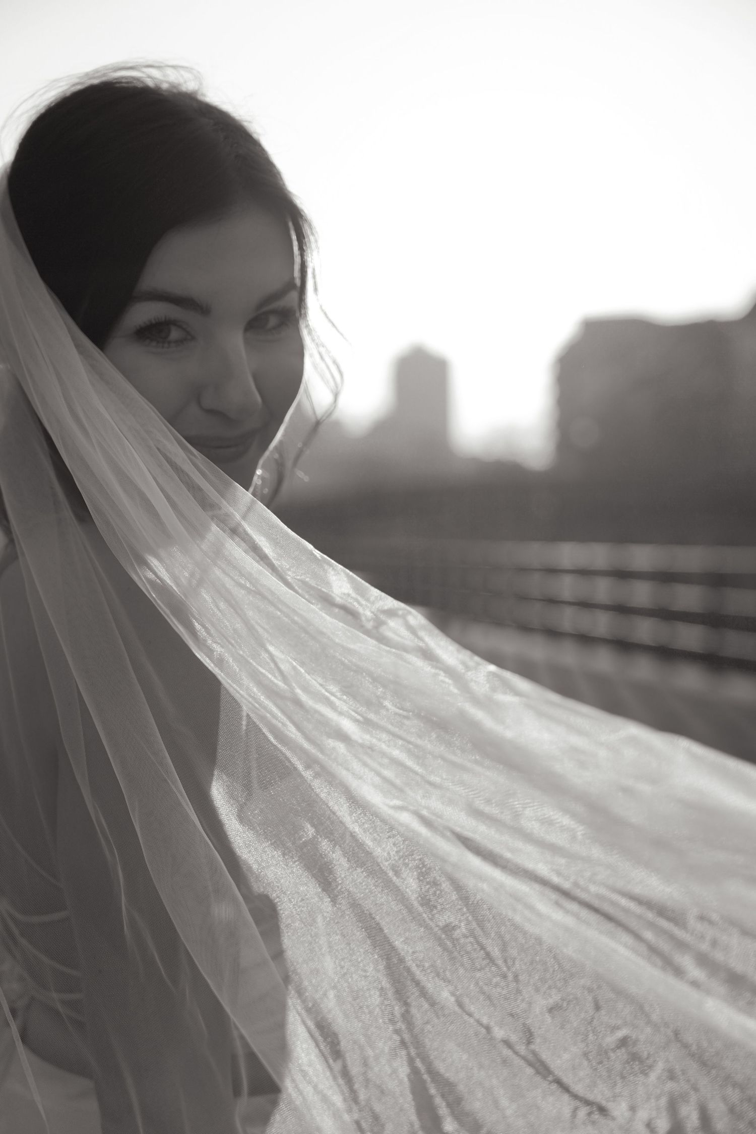 Artistic black and white portrait with flowing bridal veil against city skyline.