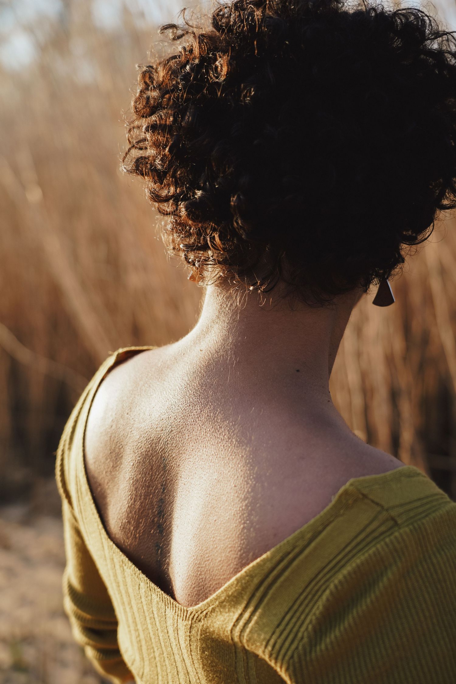 Back view portrait showing curly hair and olive green top in natural lighting.
