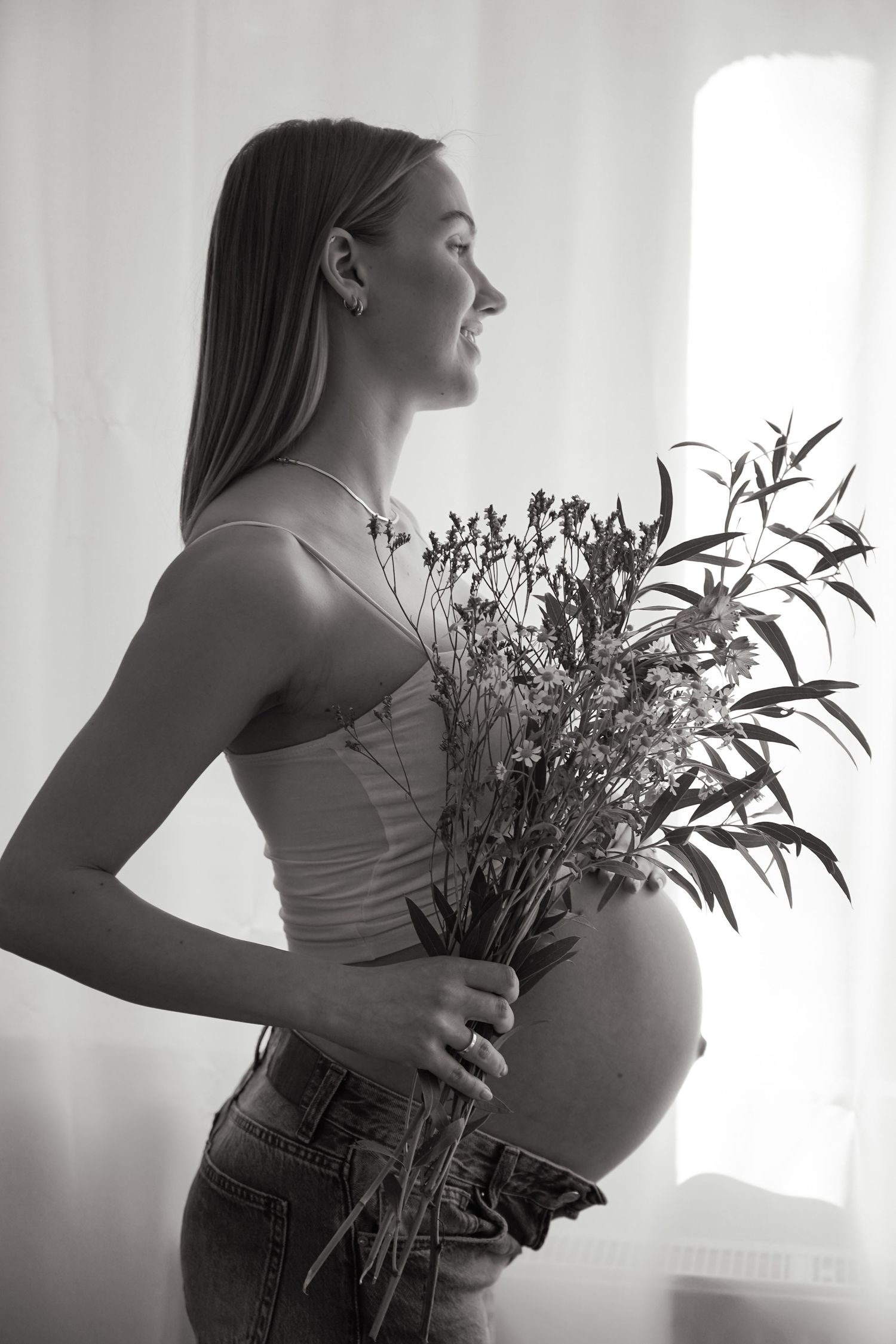 Silhouetted maternity portrait of expectant mother holding wildflowers by window.