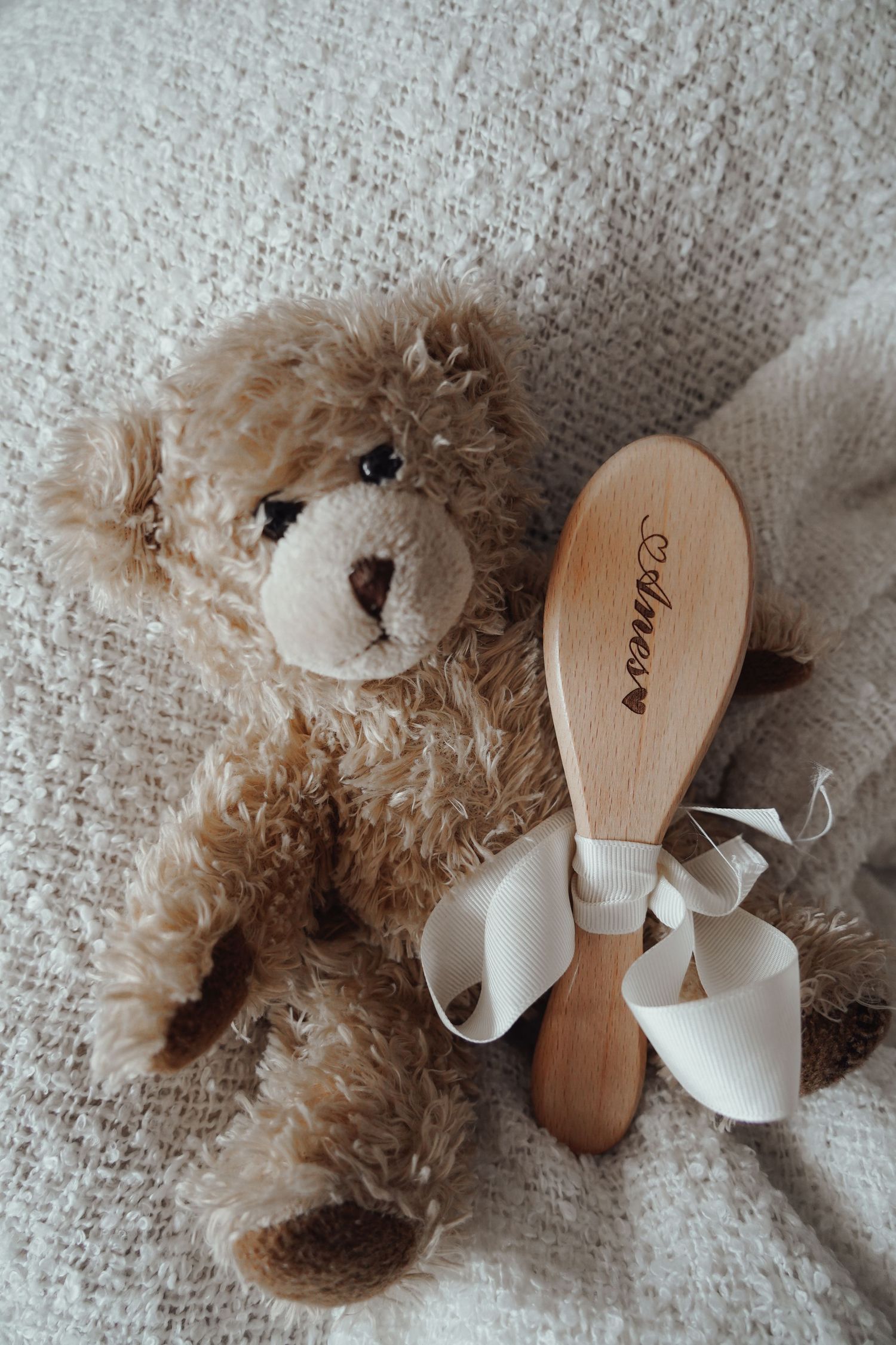 Still life with plush teddy bear and wooden hairbrush on textured fabric.