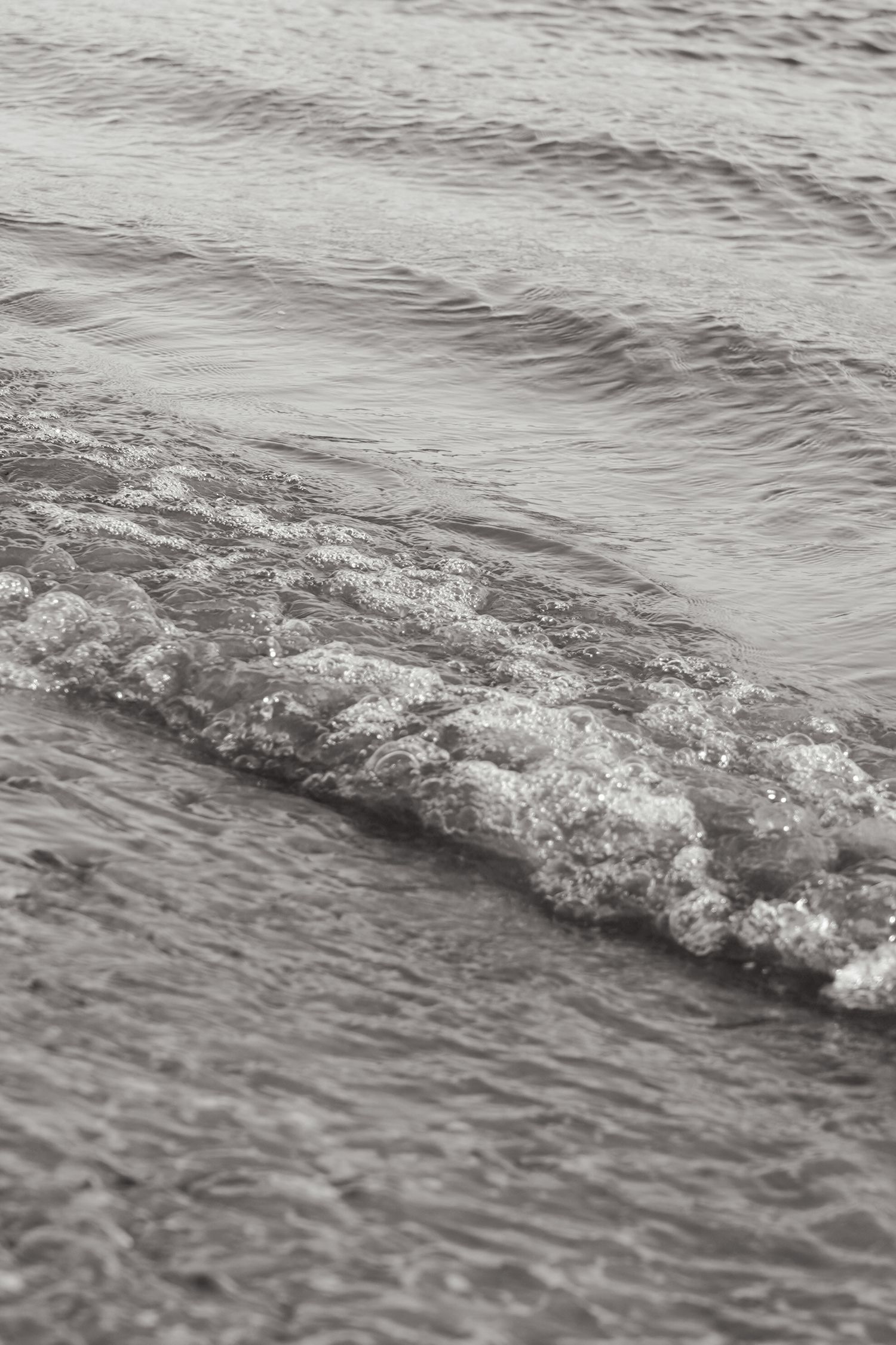 Close-up black and white photograph of gentle ocean waves rolling onto shore.