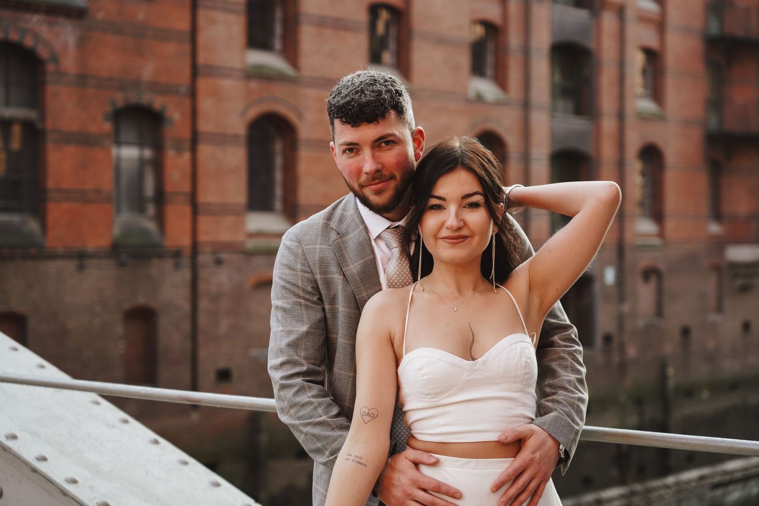 Romantic couple pose together on urban bridge with brick building backdrop.