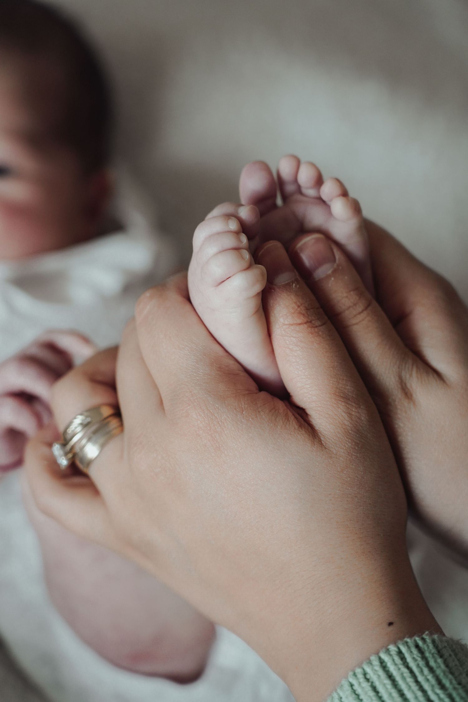 Gentle hands hold tiny baby feet against a soft white background.
