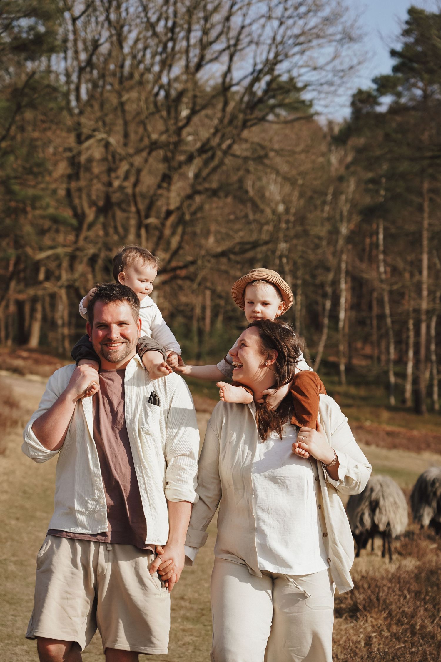Family wearing coordinated white and beige outfits enjoy a sunny day together in a wooded outdoor setting.