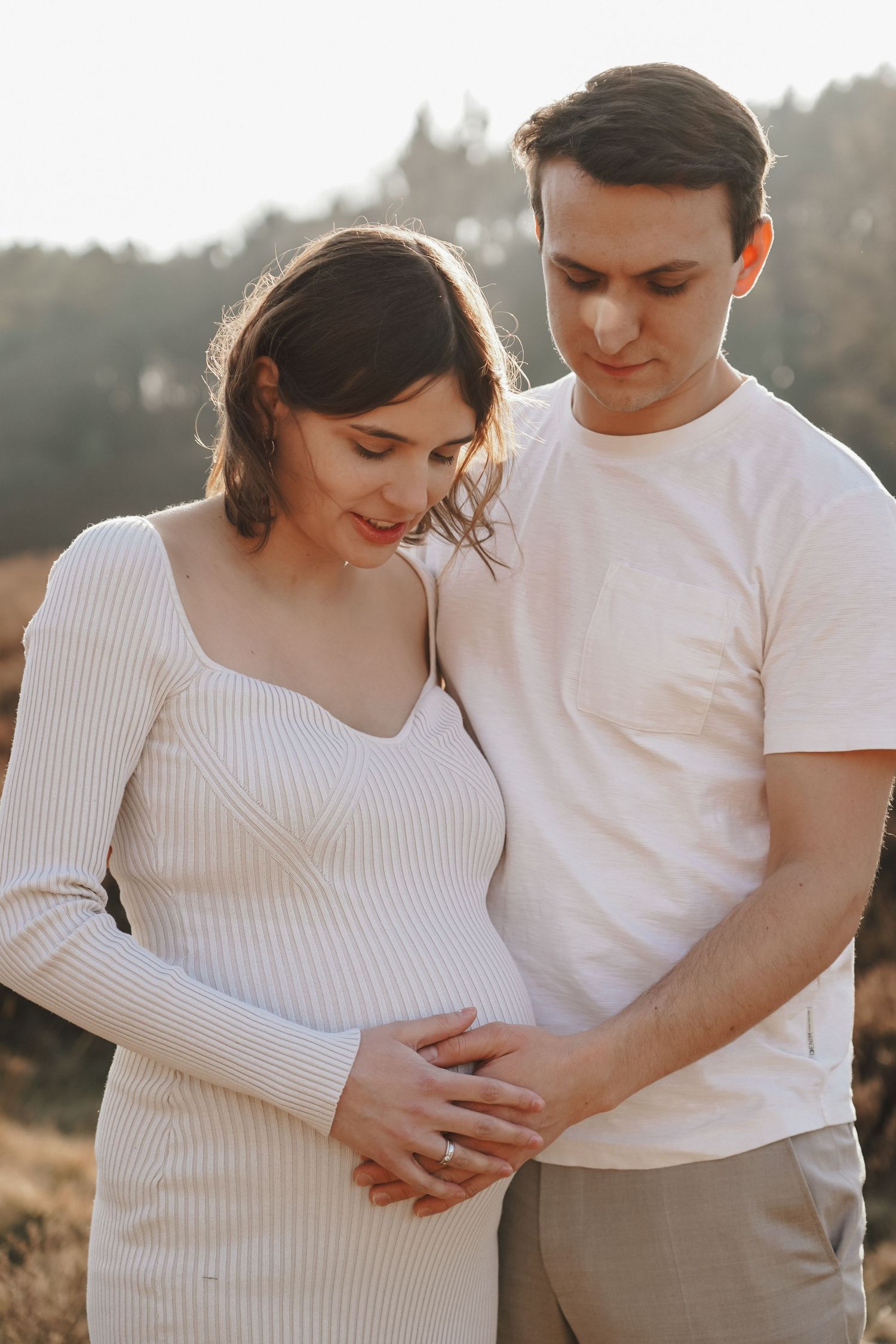 Intimate outdoor maternity photo showing couple embracing against natural backdrop at sunset.