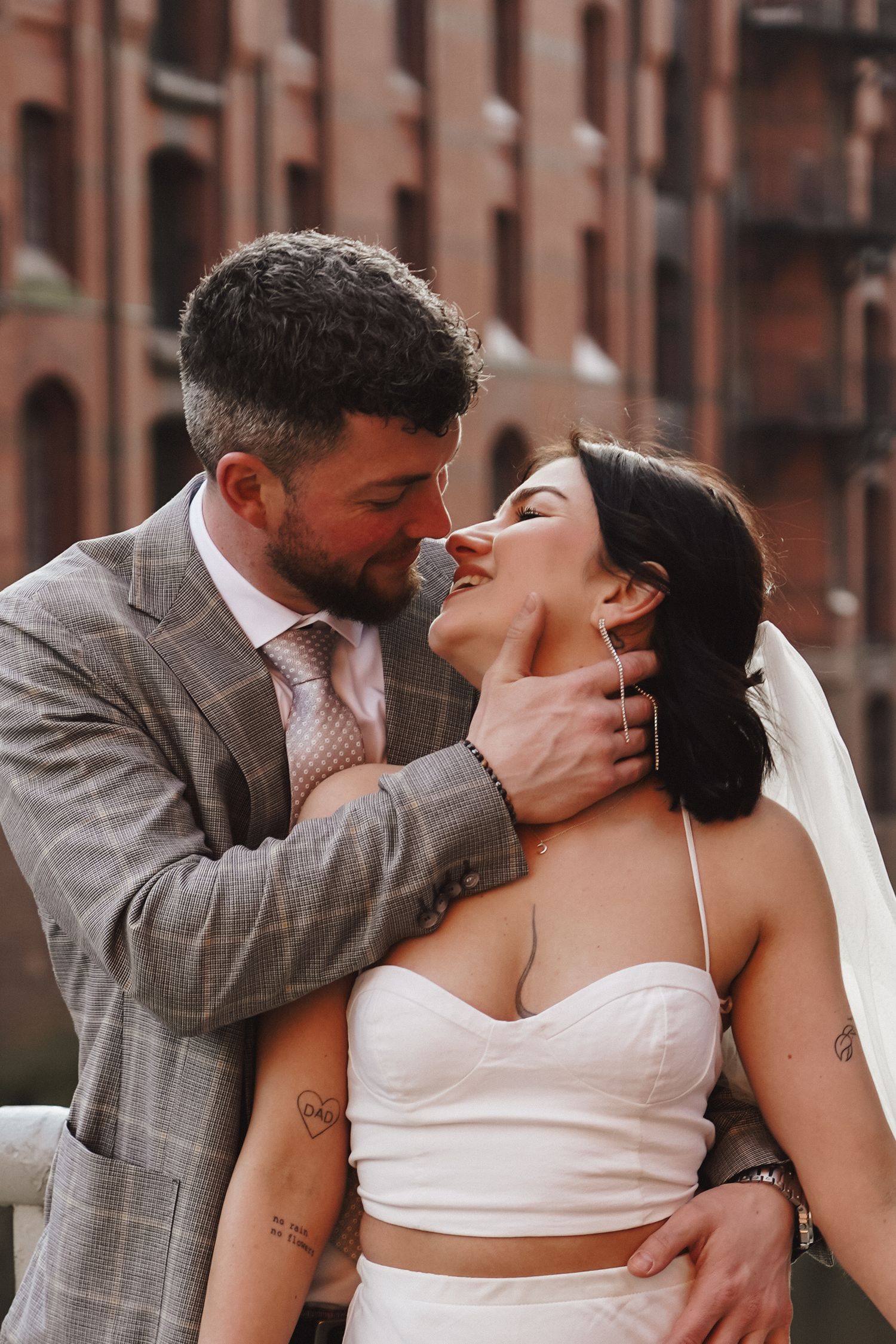 Intimate moment between newlyweds with bride in modern two-piece dress against urban setting.