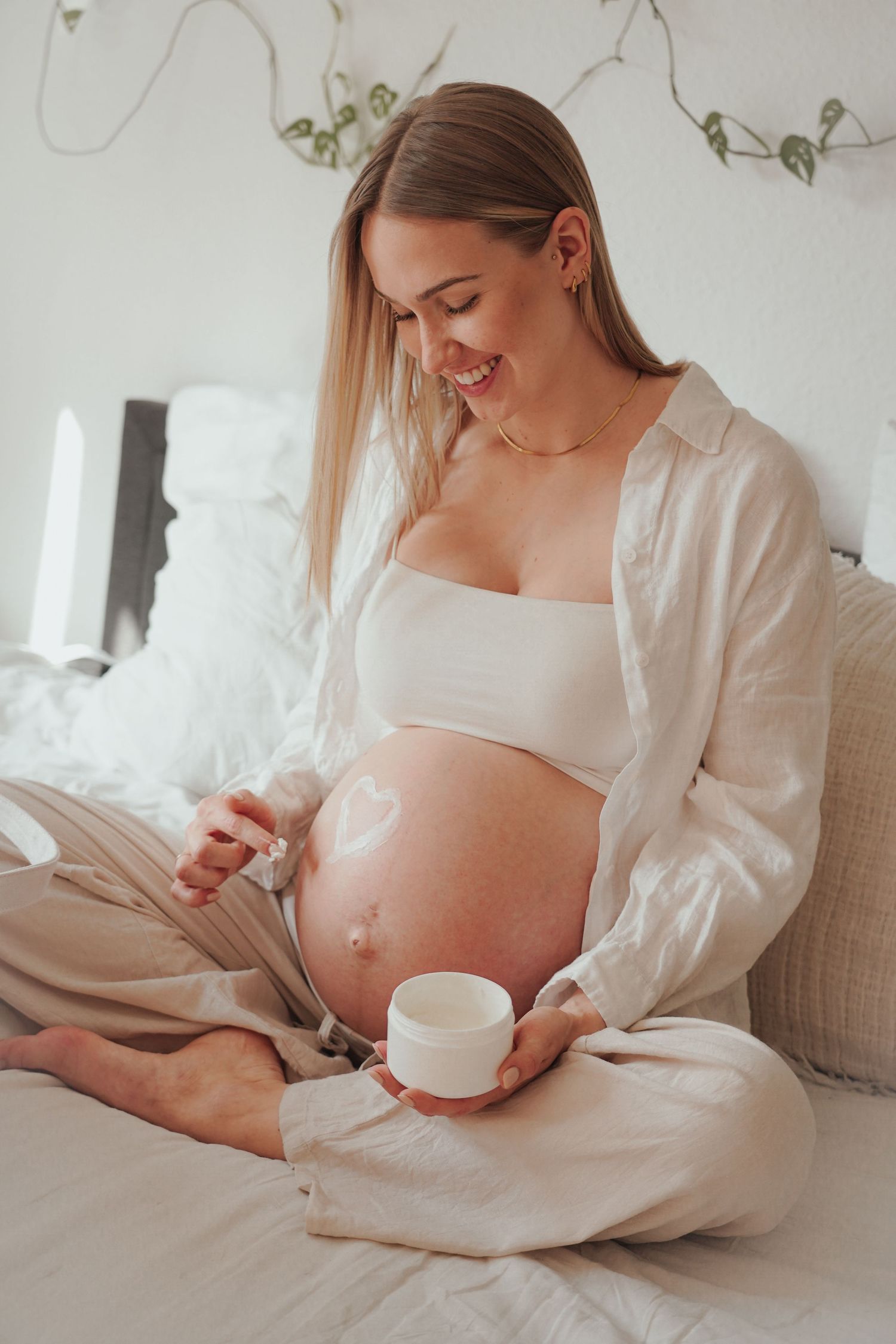 Cozy maternity photo of expectant mother enjoying tea in white bedding.
