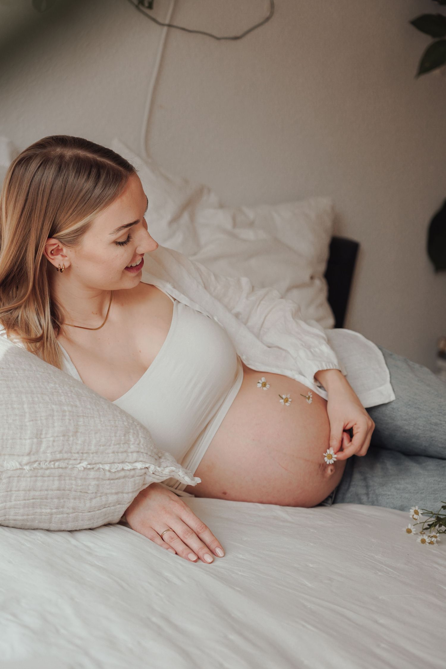 Intimate maternity photo showing a woman resting on white bedding with hand on her belly.