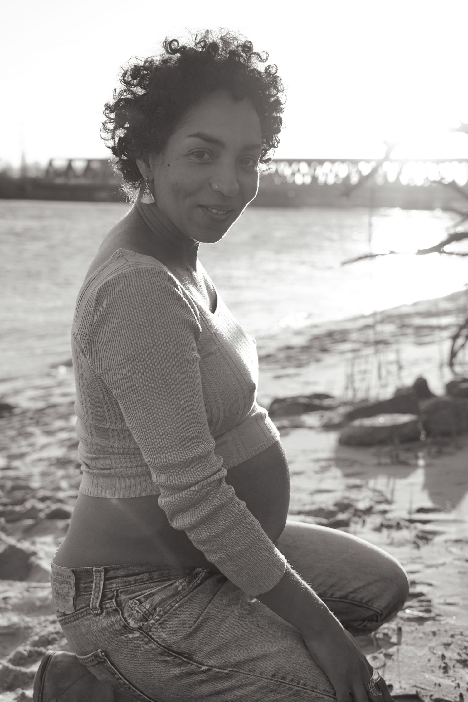 Black and white maternity portrait by waterfront with natural lighting.