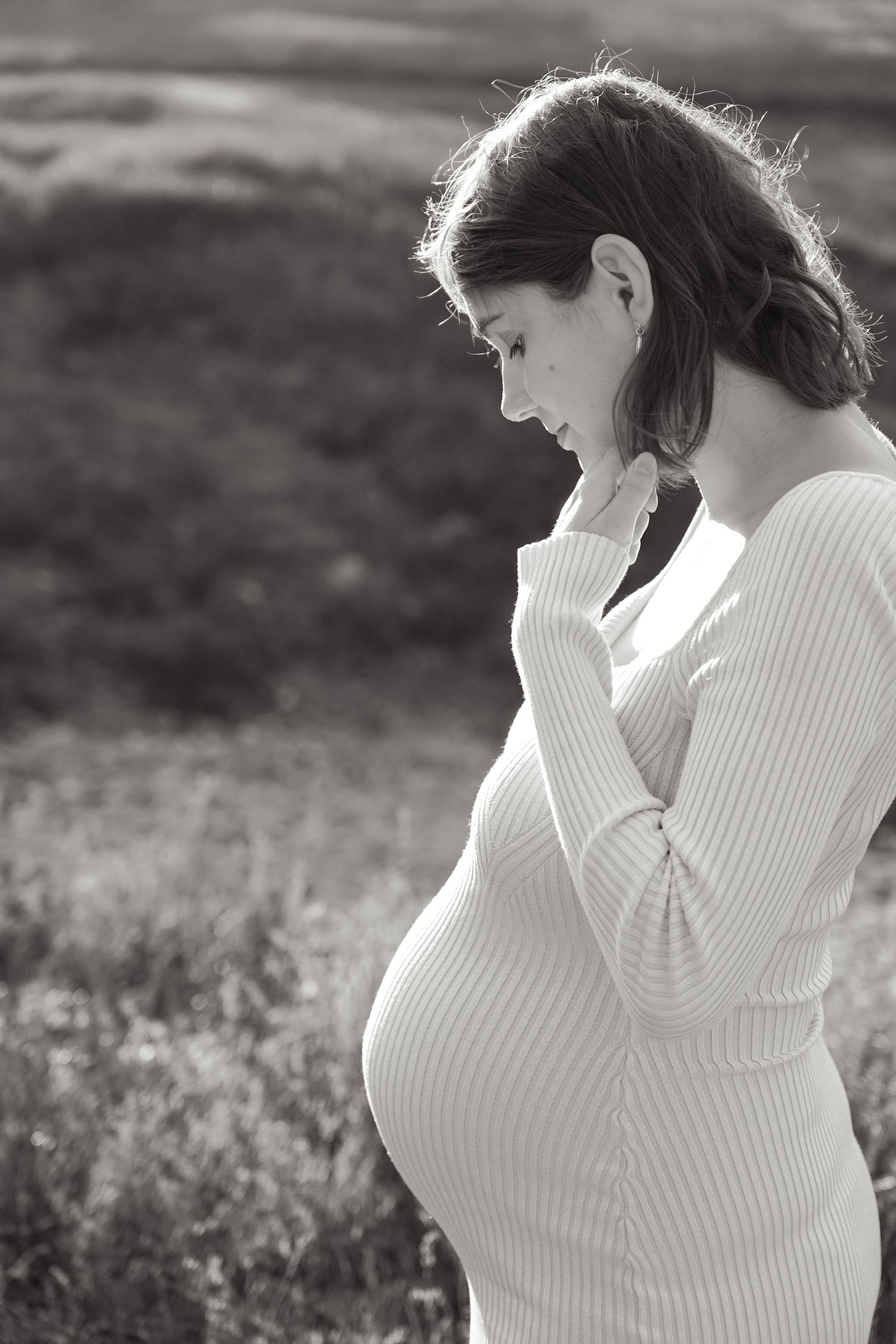 Side profile of pregnant woman in white sweater standing in natural light.