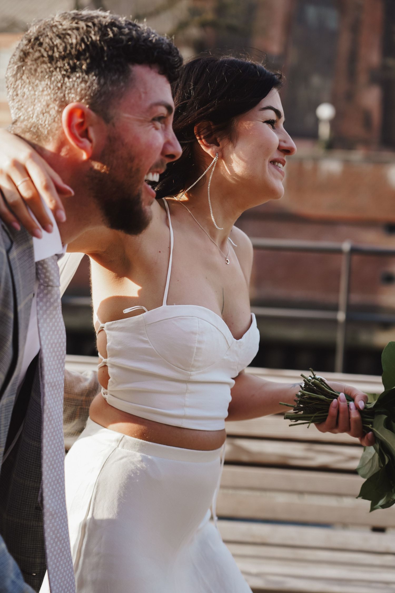 Happy wedding couple share intimate moment outdoors with brick building backdrop.