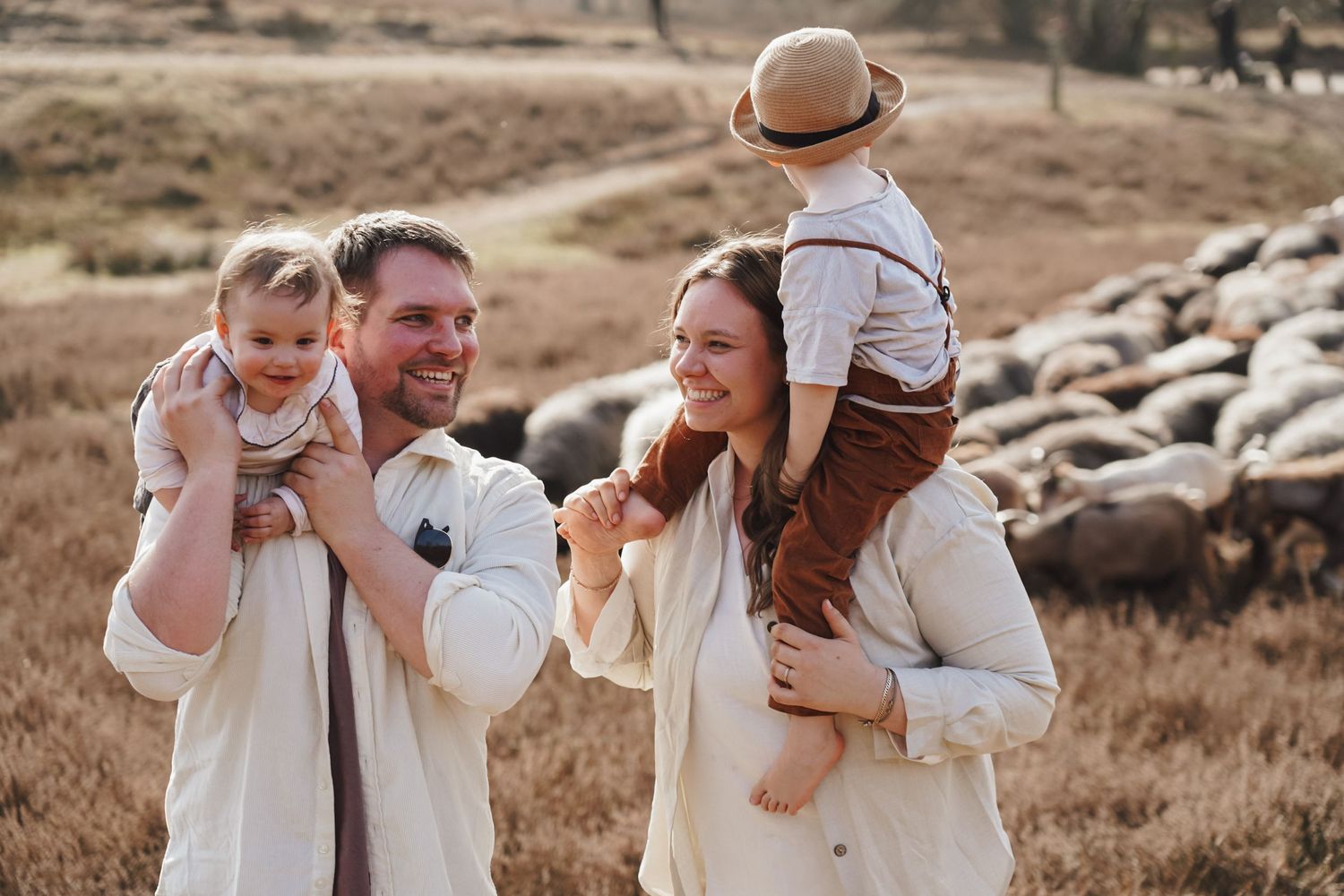 Happy family sharing laughter and joy together outdoors with sheep grazing in the background.