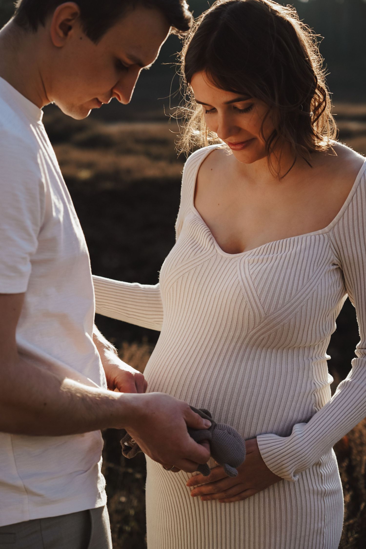 Intimate maternity photoshoot at sunset with couple in white outfits.