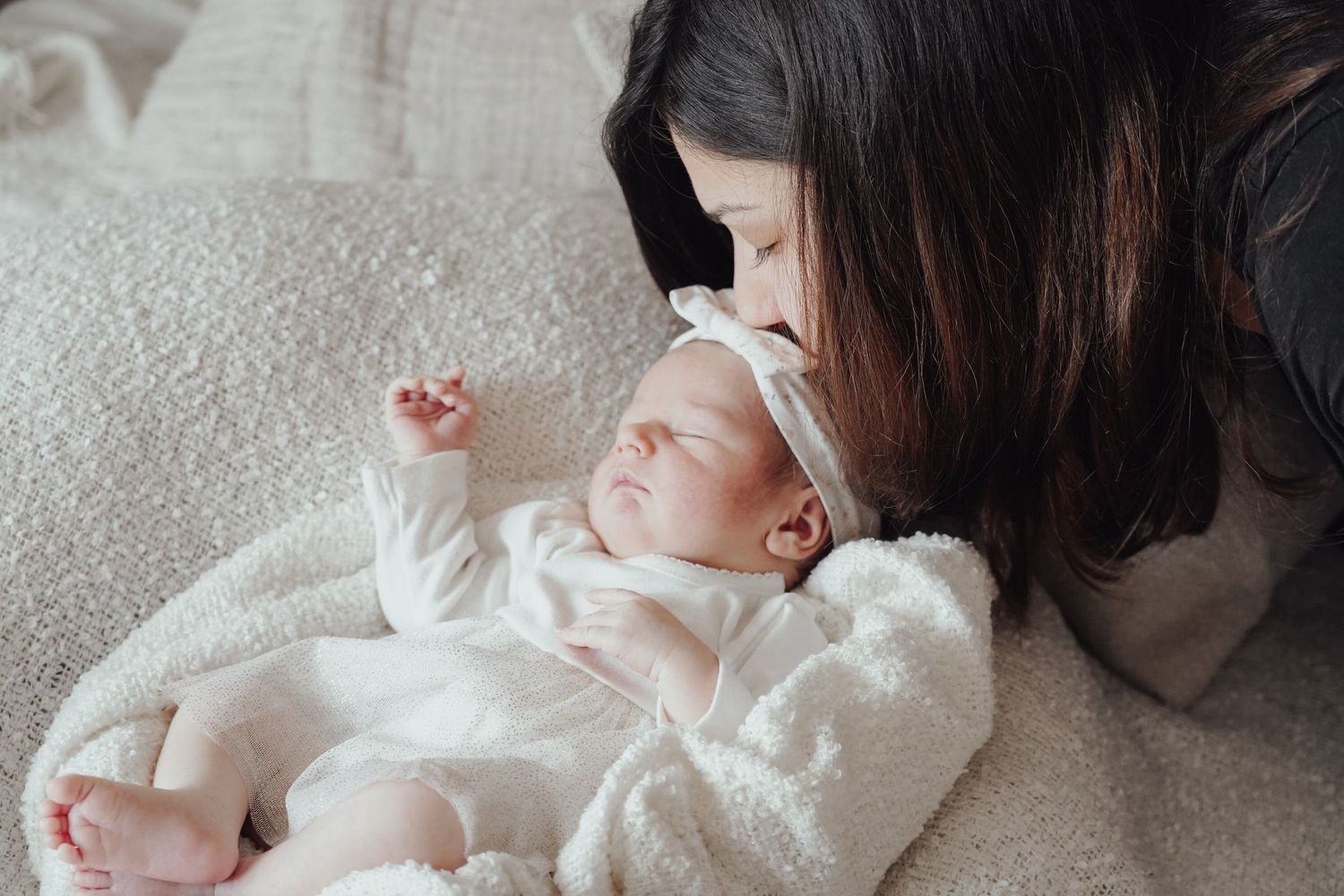 A tender moment with a sleeping infant wrapped in white on a cozy blanket.