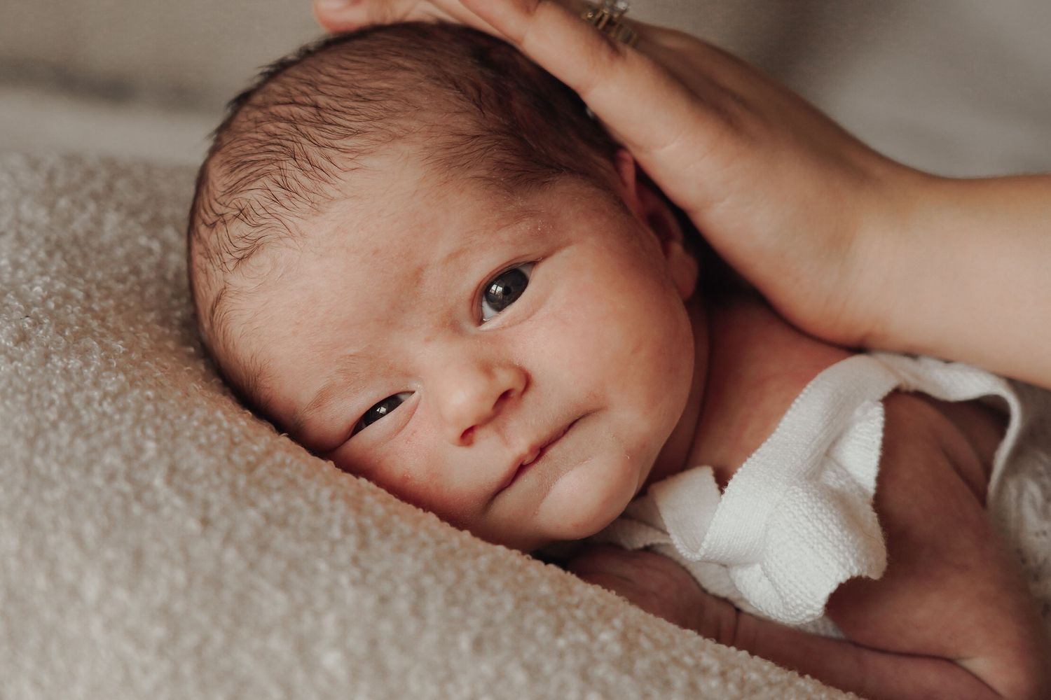 Newborn baby resting on soft fabric with gentle hand touching their head.