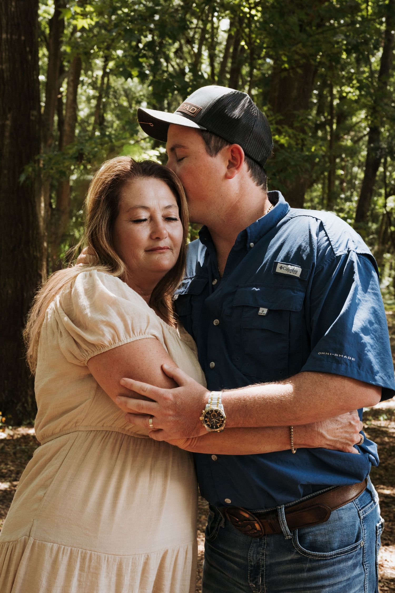 Portrait of mother and son side hugging as son is kissing mom's head and mom has eye's closed with a slight smile.