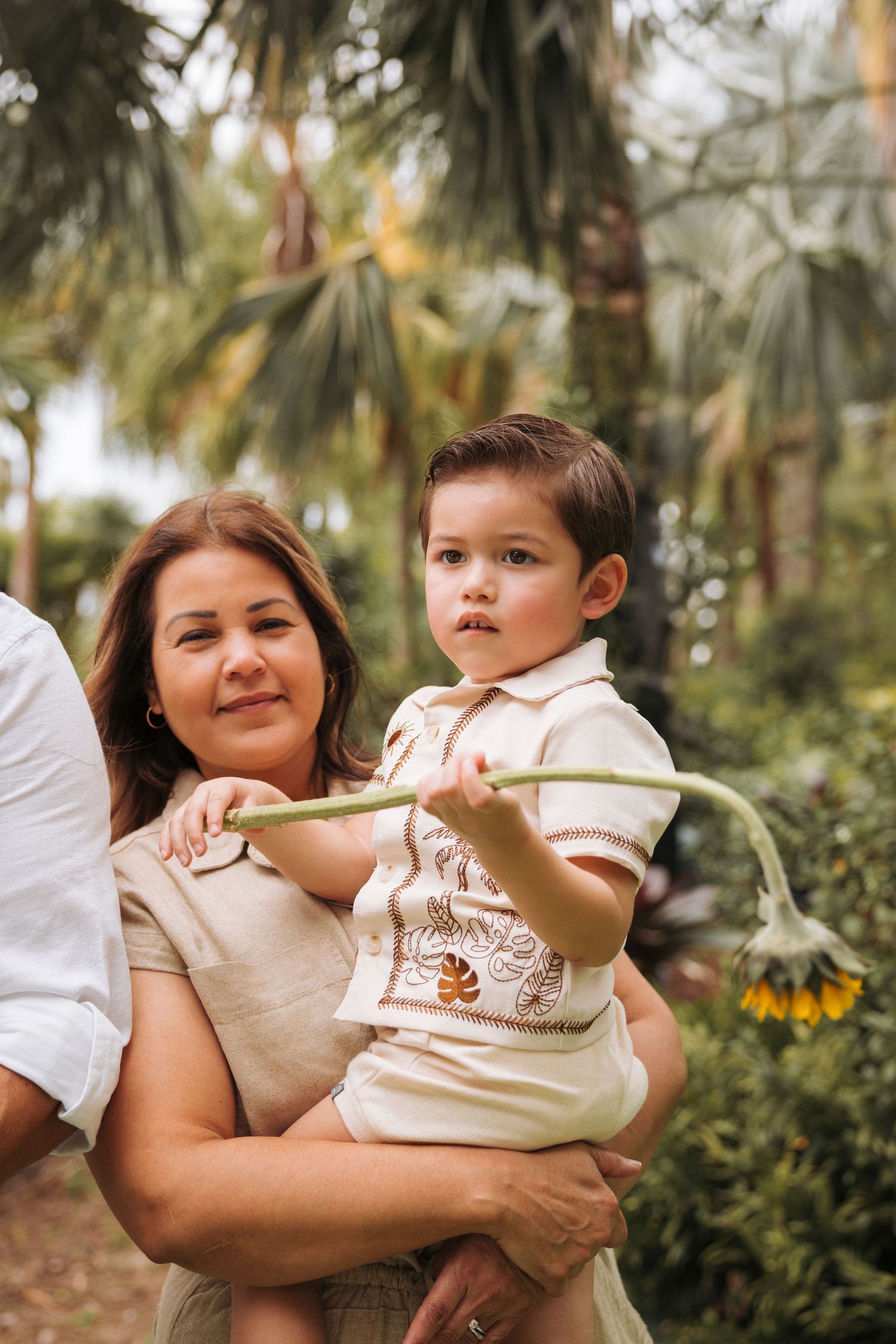 Close up of a family portrait. Grandmother is holding grandson while he looks off to the side holding a sunflower.